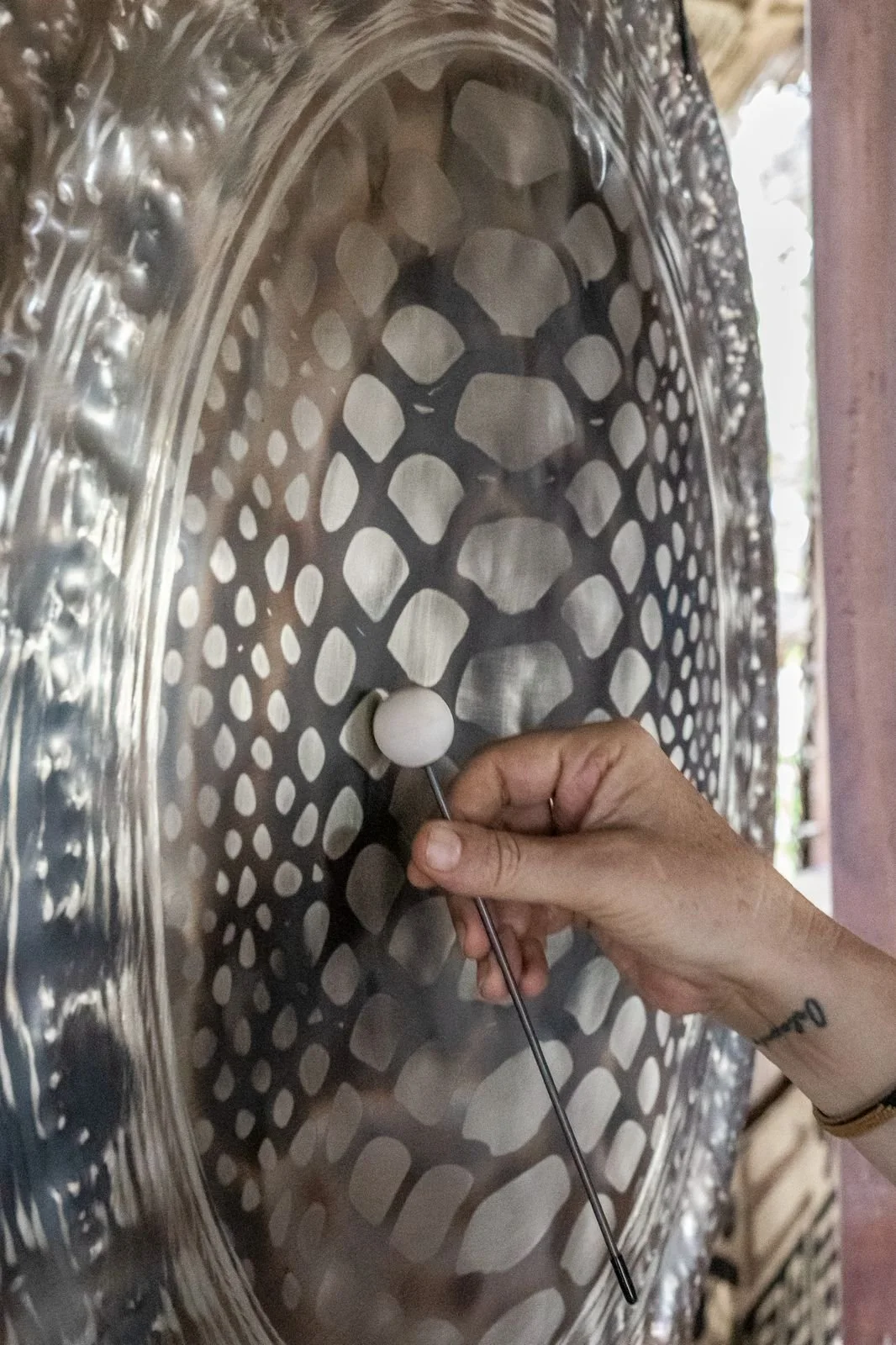 A person's hand is placing a white ball into a metal drum with a perforated pattern, possibly for milling or grinding.