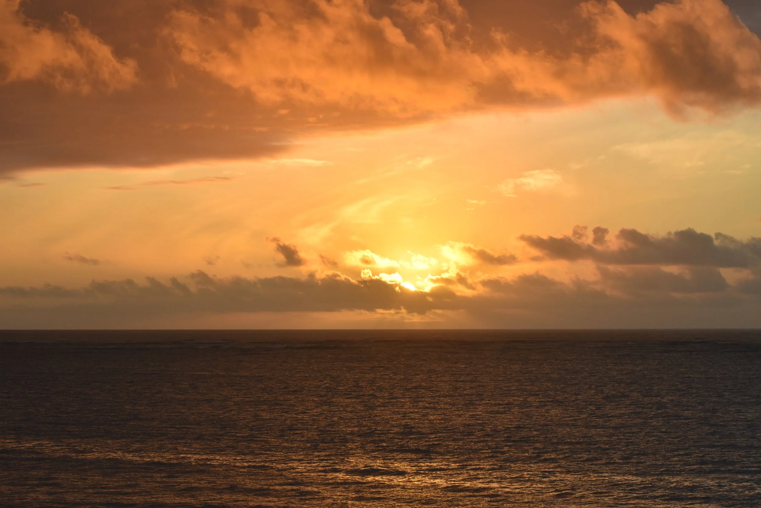 A sunset over the ocean with orange and yellow clouds in the sky.