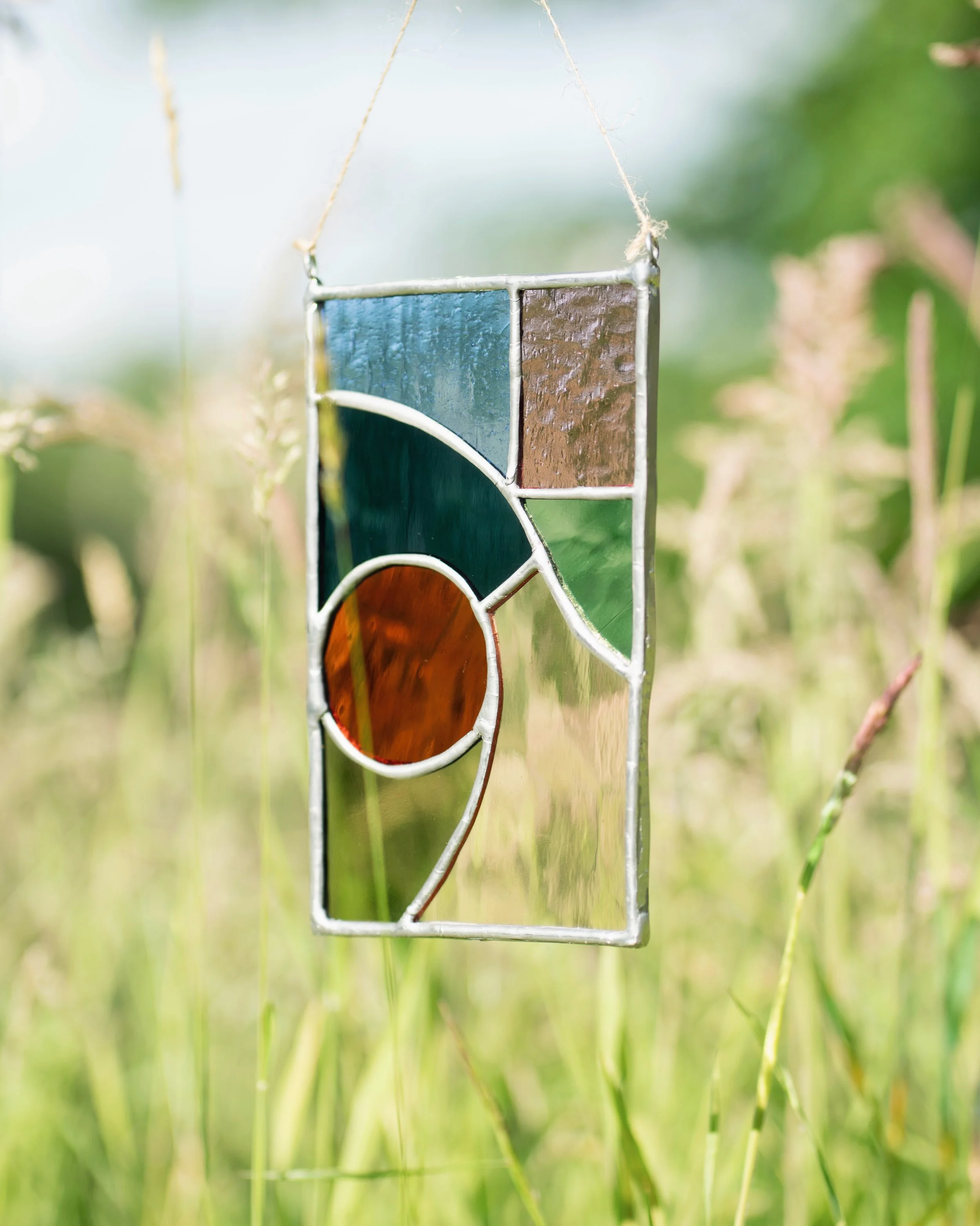 Close-up of a stained glass panel hanging outside against green grass with a blurry natural background.