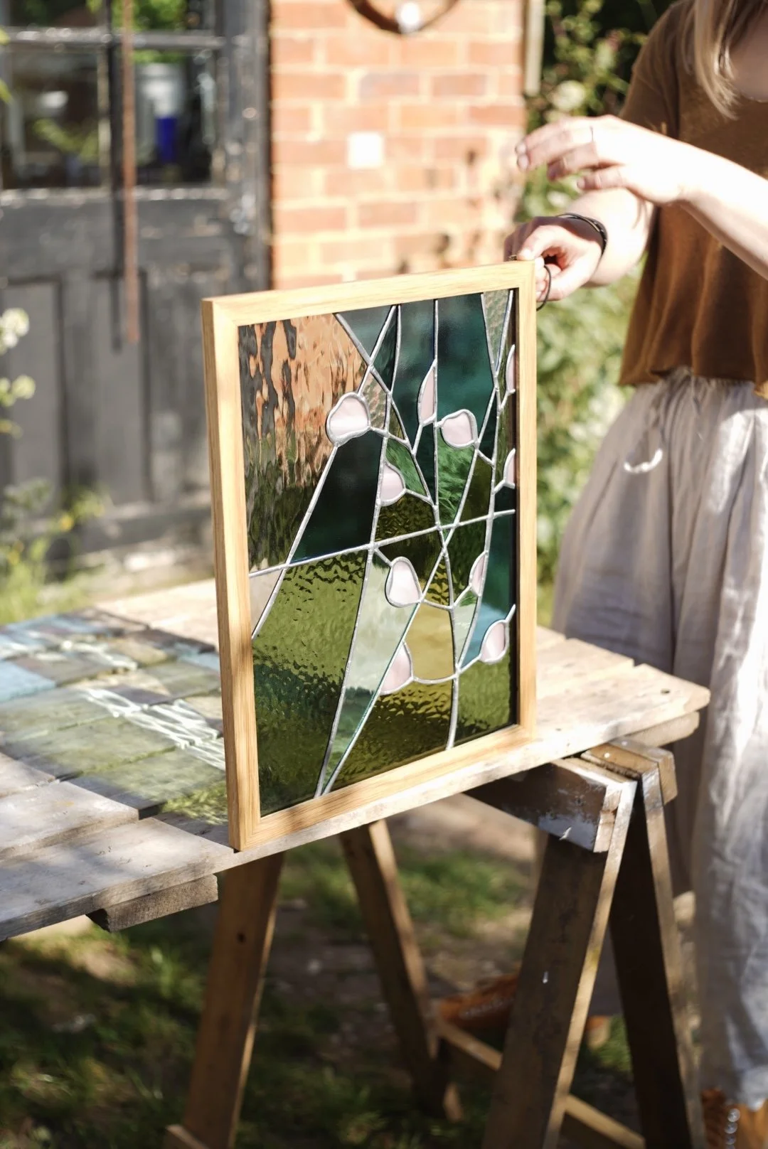Person holding a framed stained glass art piece outdoors on a table.