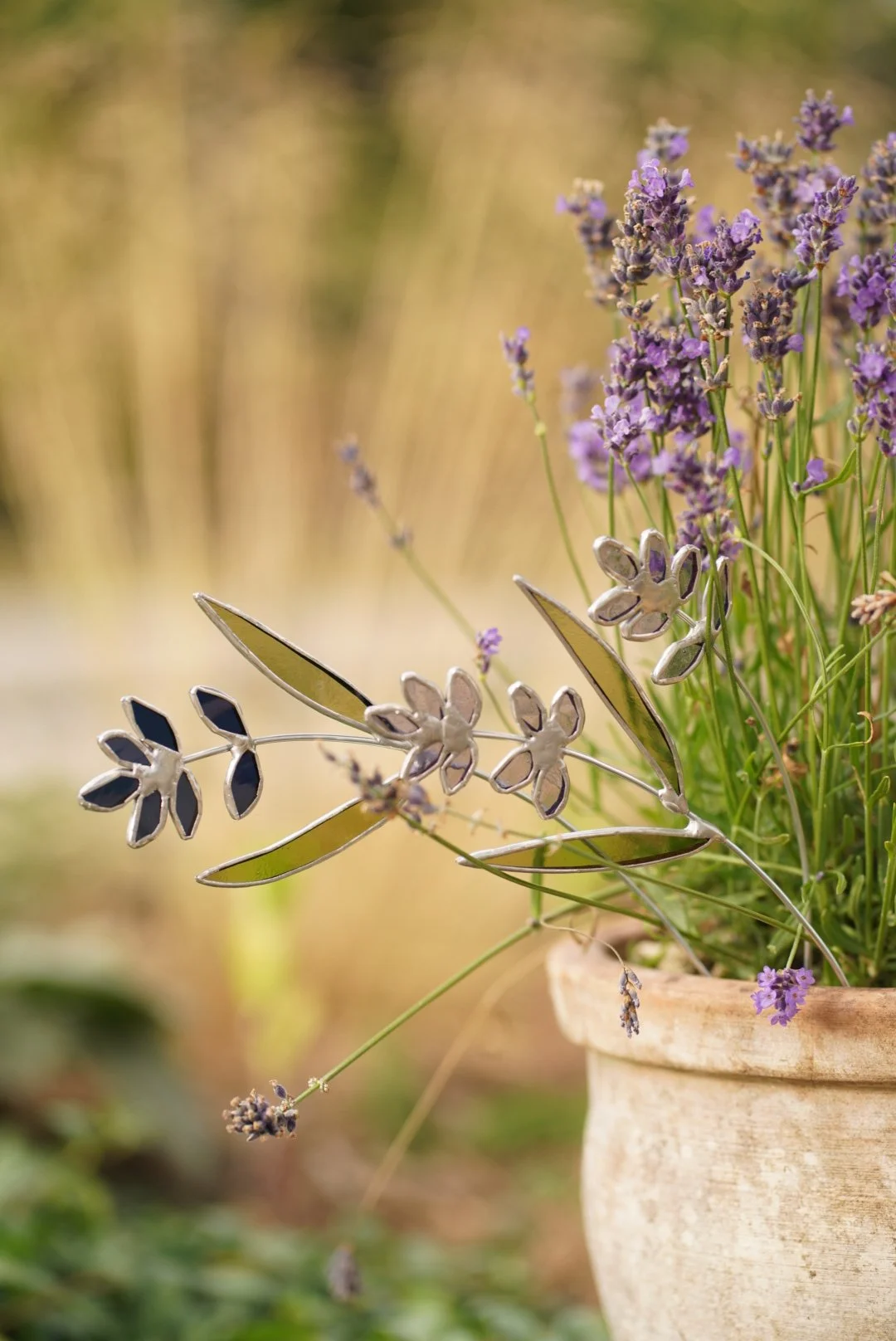 Purple lavender flowers in a terracotta pot with decorative metal butterfly and leaf ornaments.