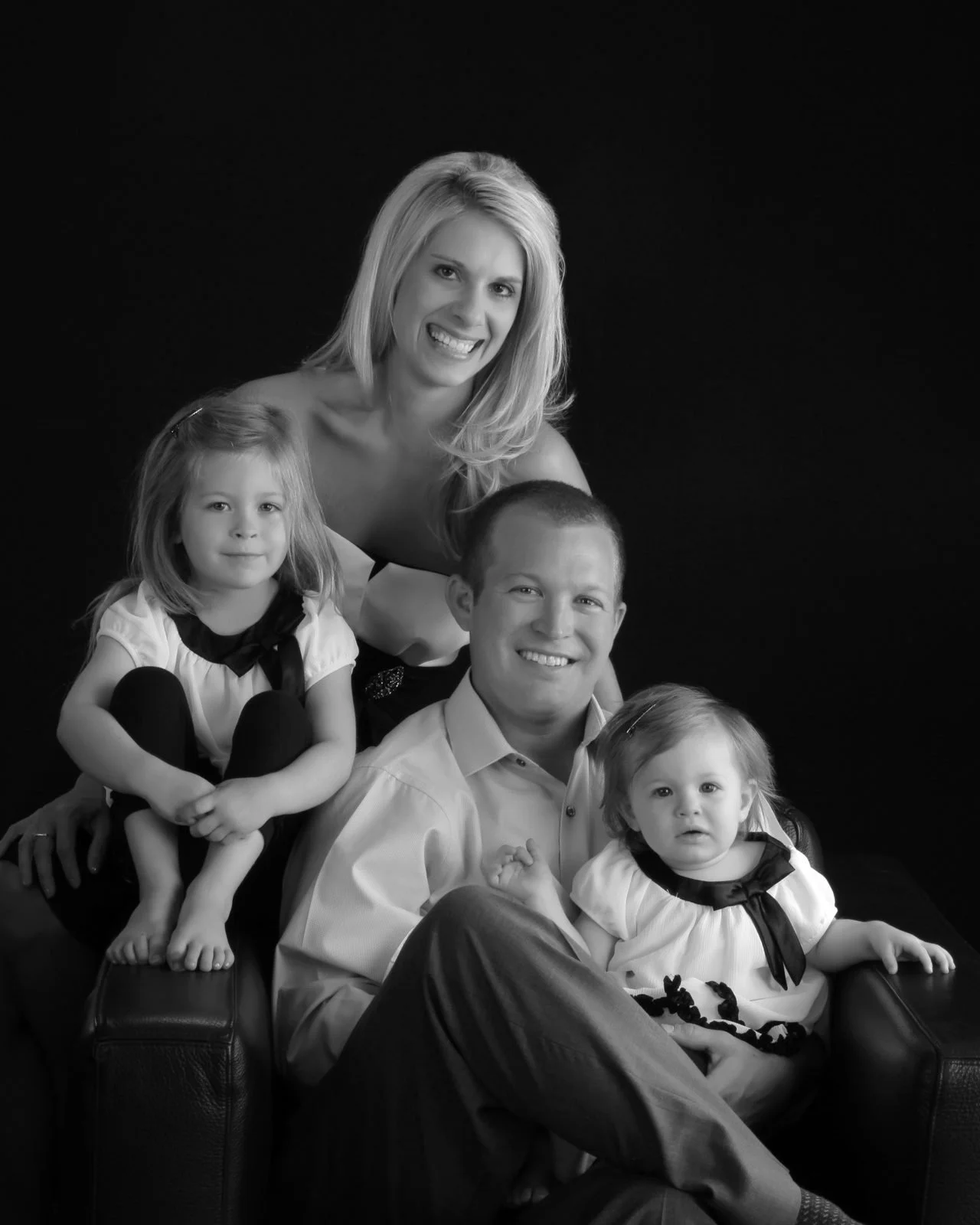 Family of five, a mother and father with three young children, posed on a black backdrop