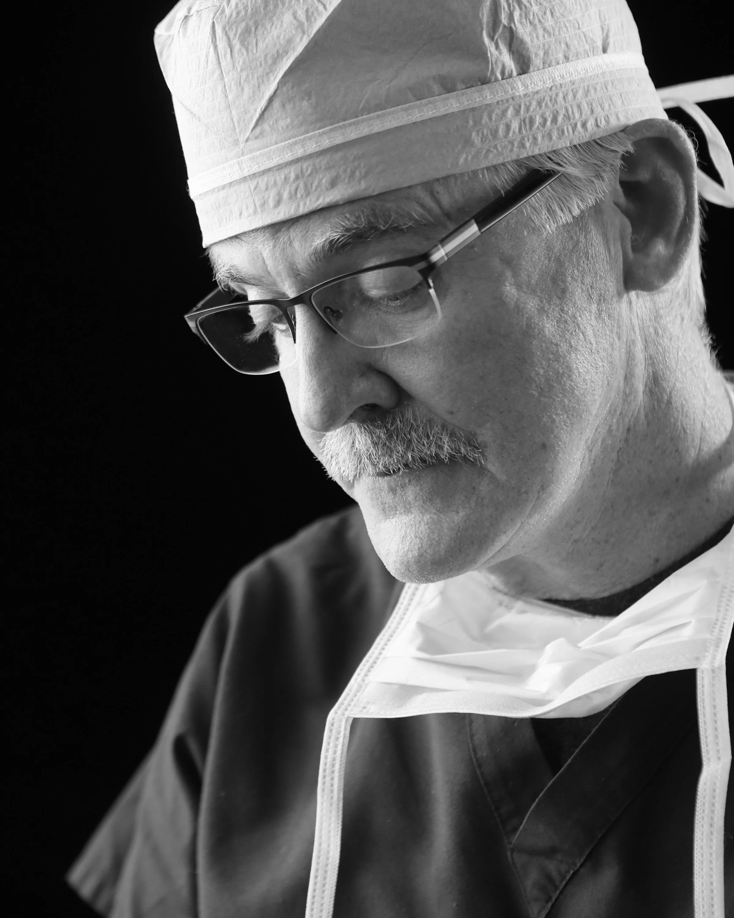 Black and white portrait of a surgeon in glasses and a surgical cap, looking down