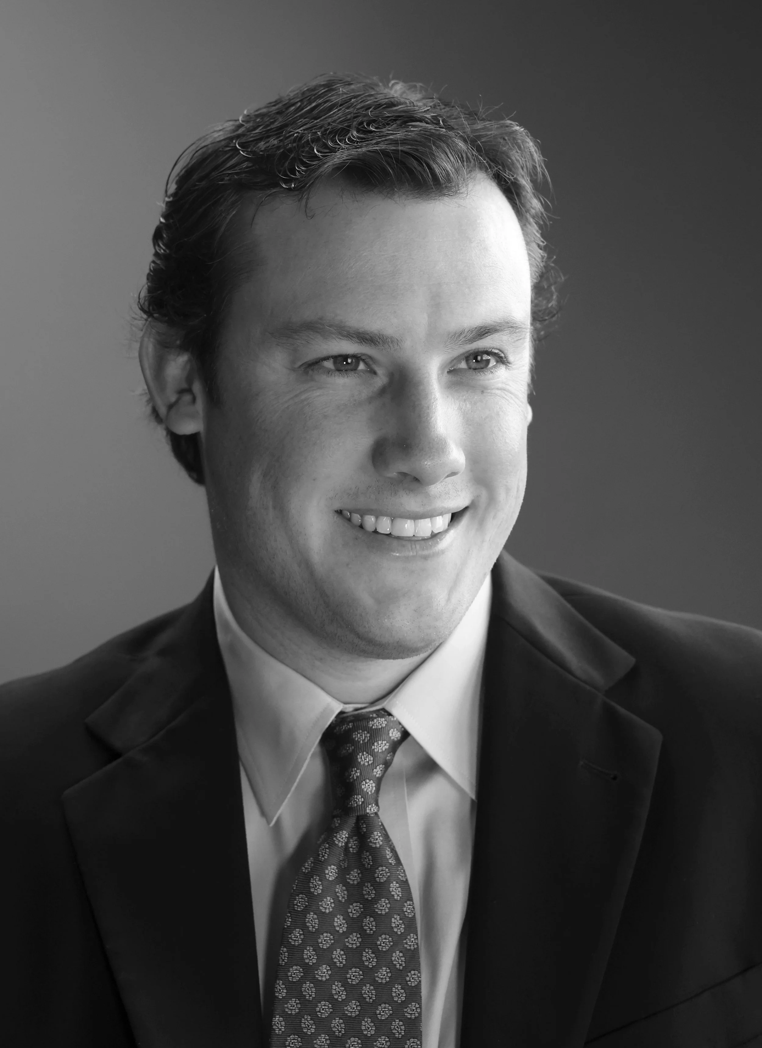 Professional black and white headshot of a smiling man in a suit and tie
