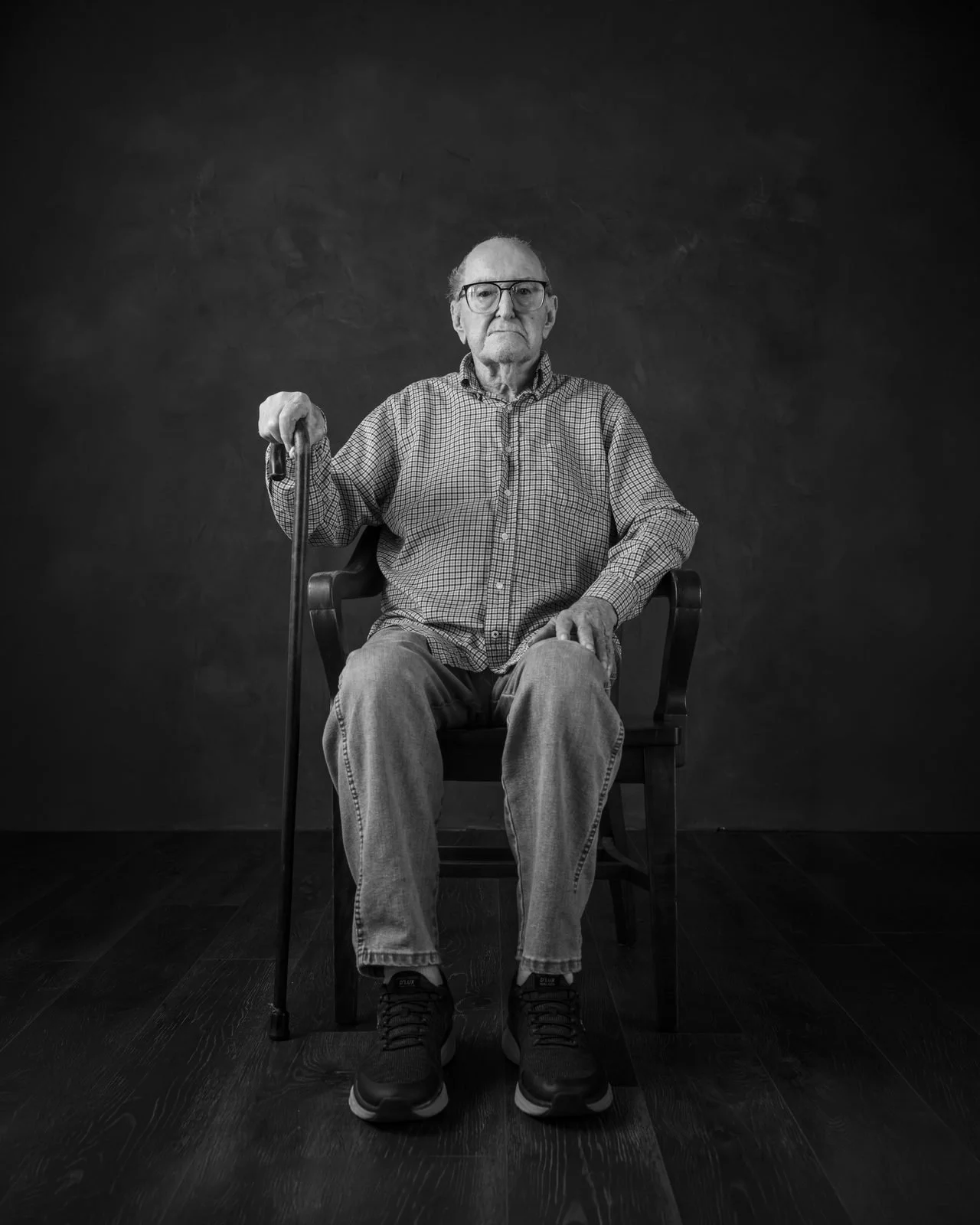 Black and white portrait of an elderly farmer seated in a wooden chair, resting his hands on a cane