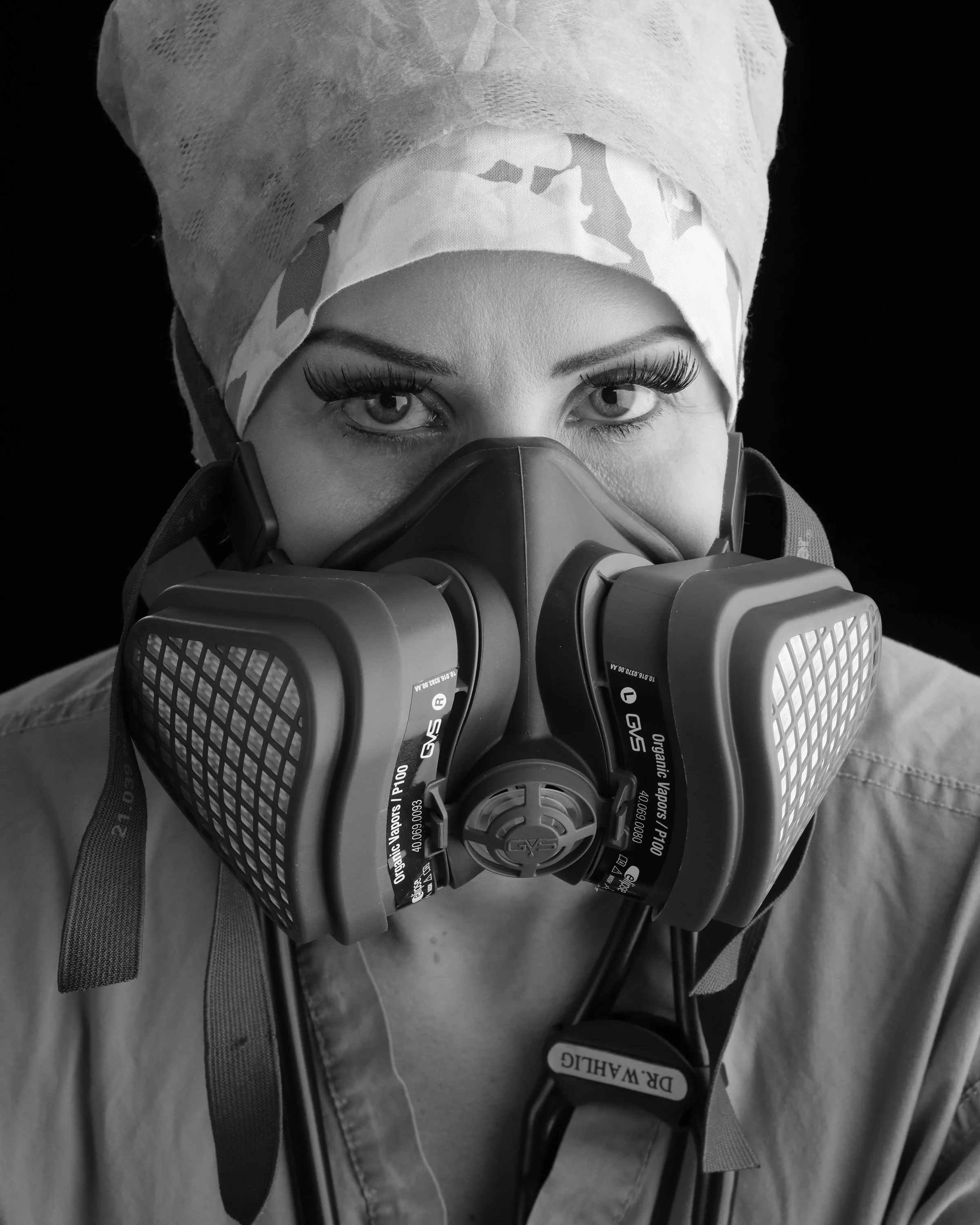 Black and white portrait of a healthcare worker in a surgical cap and respirator mask, looking at the camera