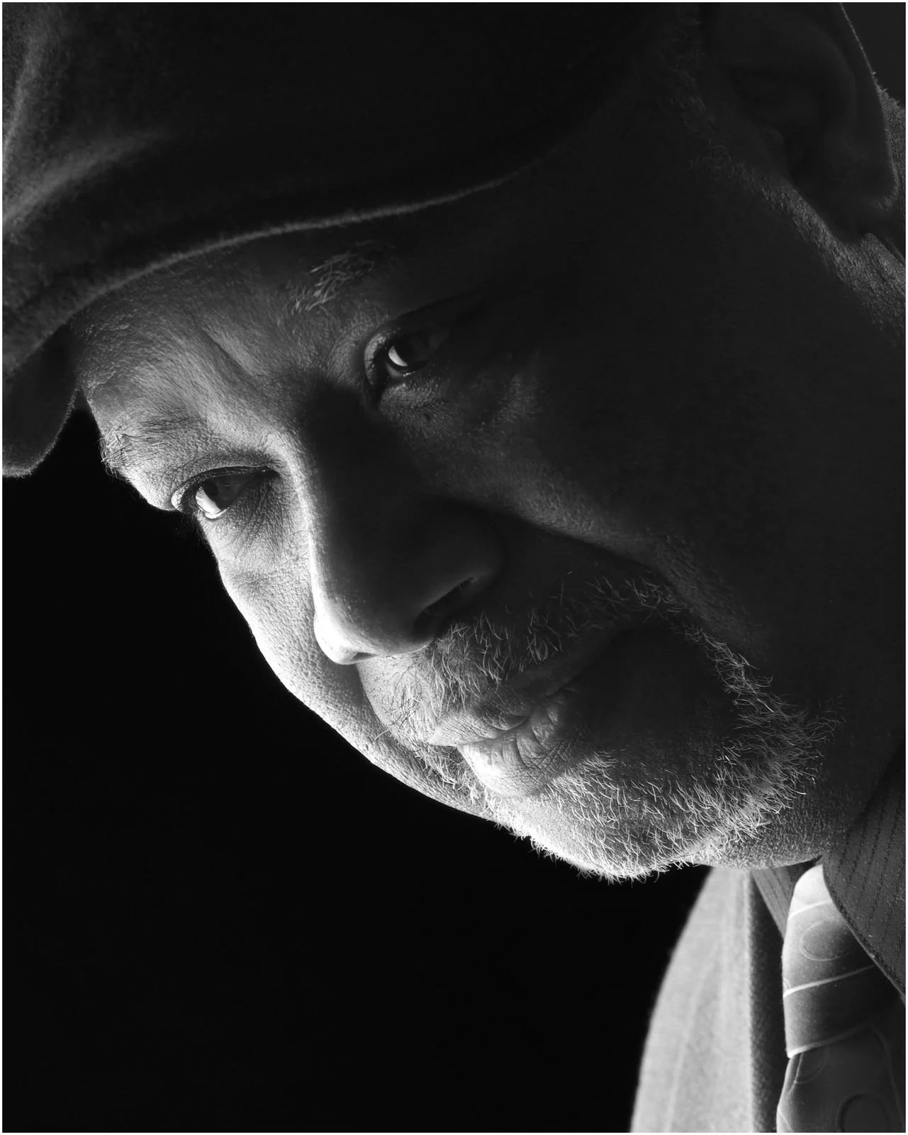 Dramatic black and white portrait of a man in a flat cap, face turned down and half in shadow
