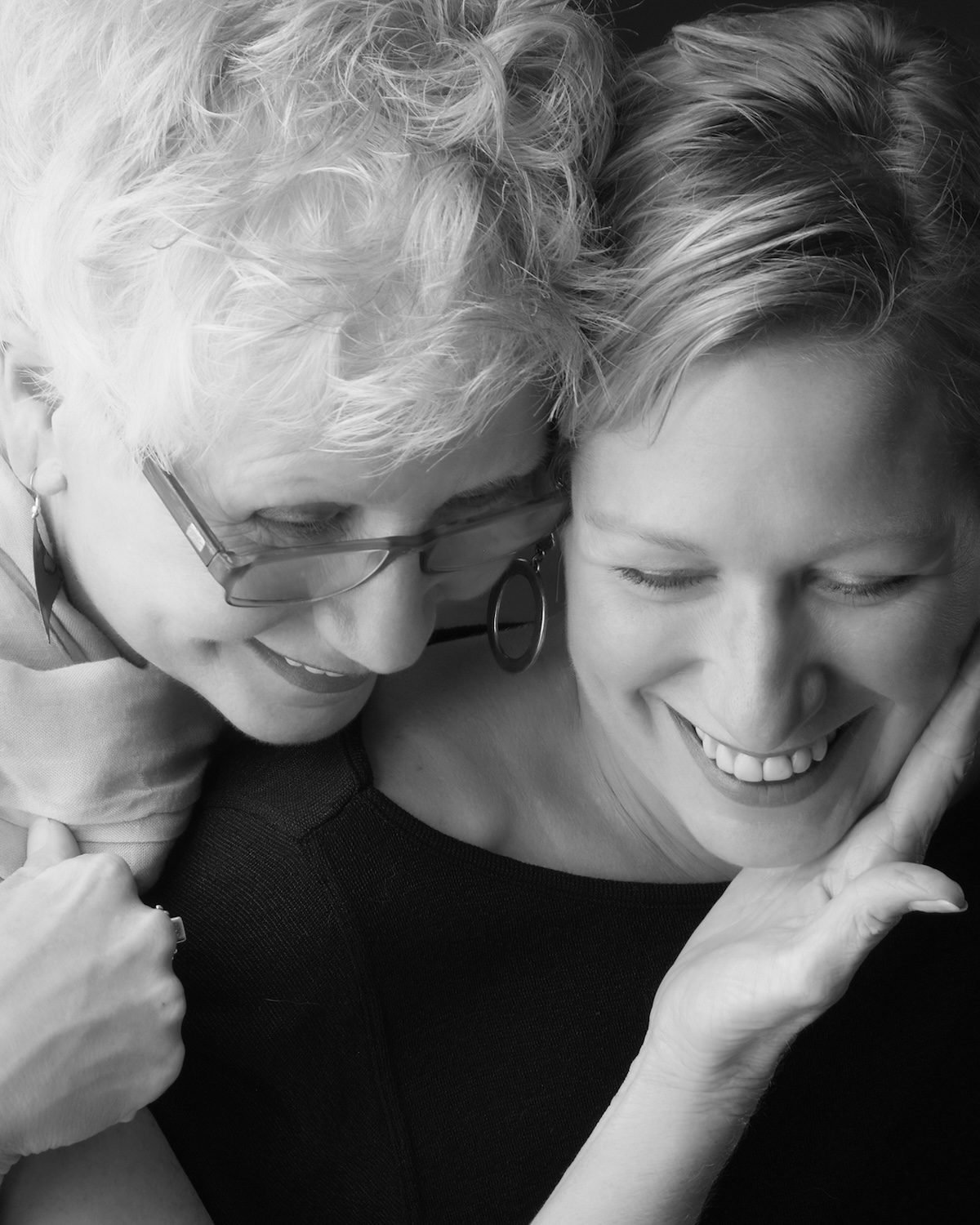 Two women laughing in an embrace with their heads together, black and white portrait