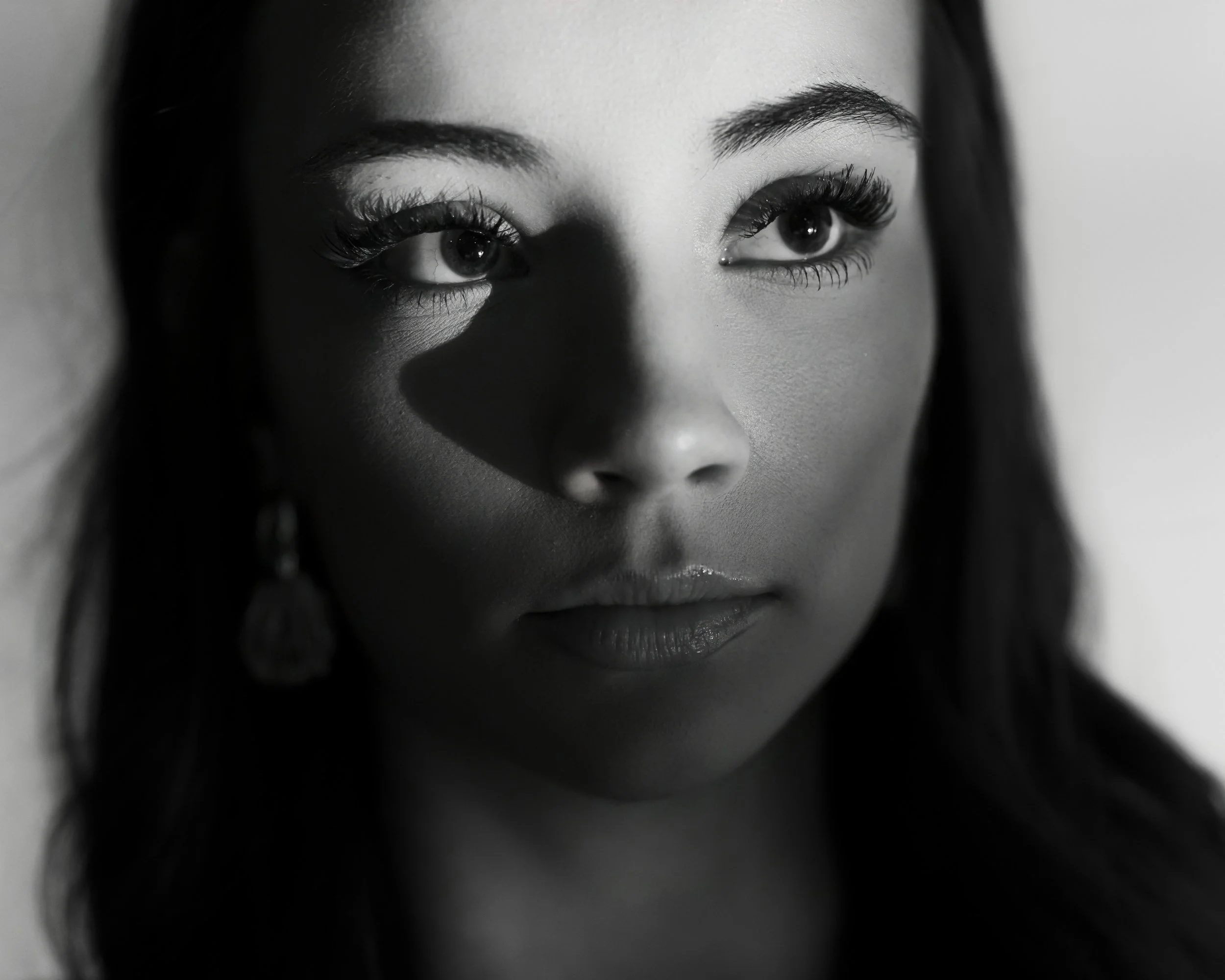 Close black and white portrait of a teenage girl with long eyelashes, her eye highlighted by a shaft of light
