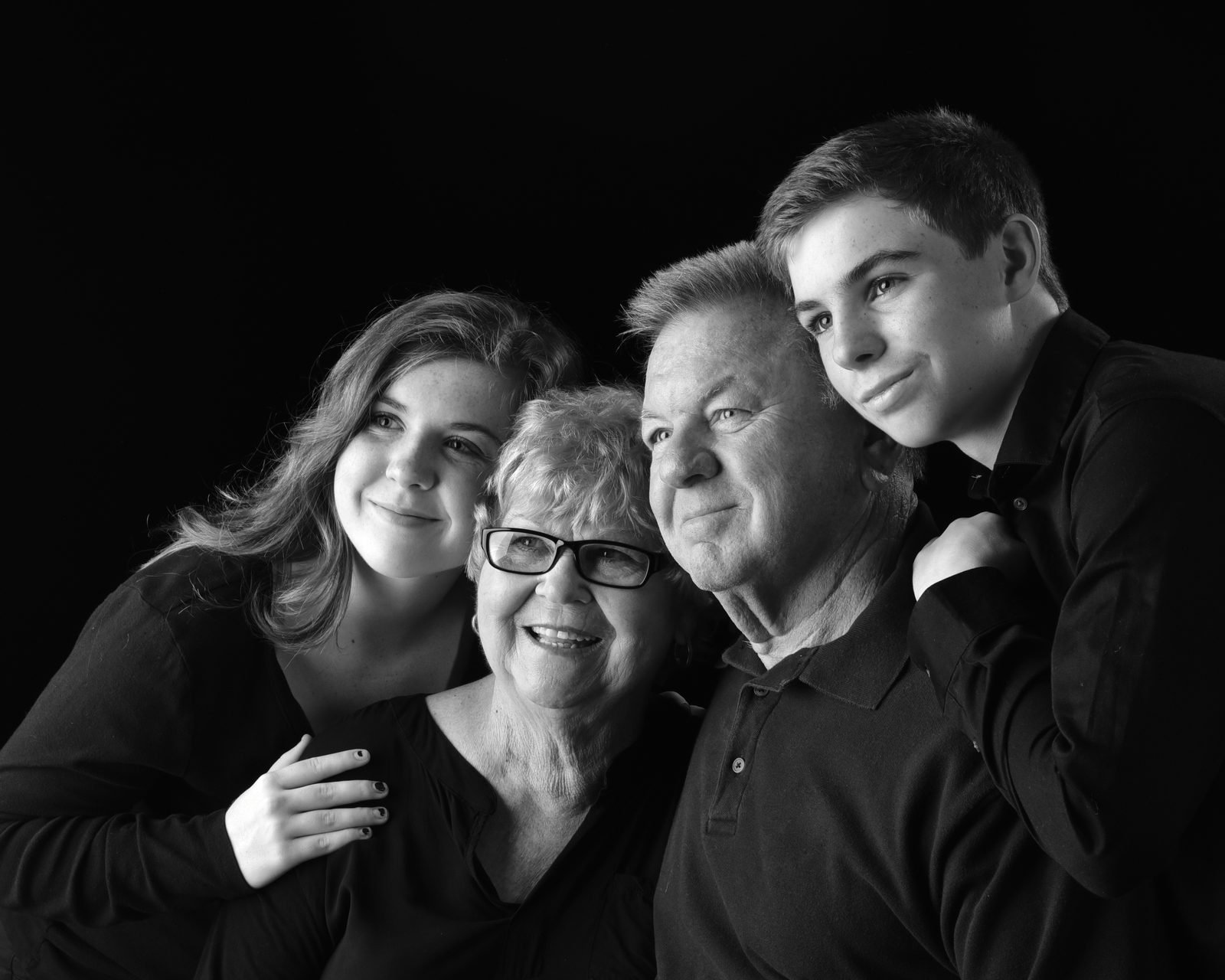 Grandparents, a daughter and two teenage grandsons posed closely together on a black backdrop, family portrait