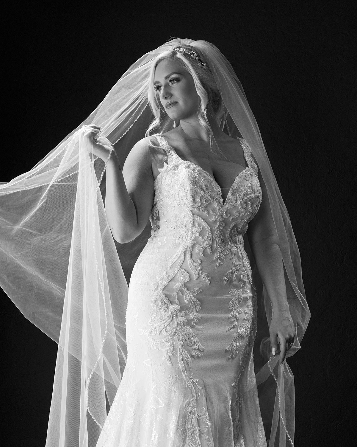 Bride in a lace gown with a sheer veil, black and white studio portrait