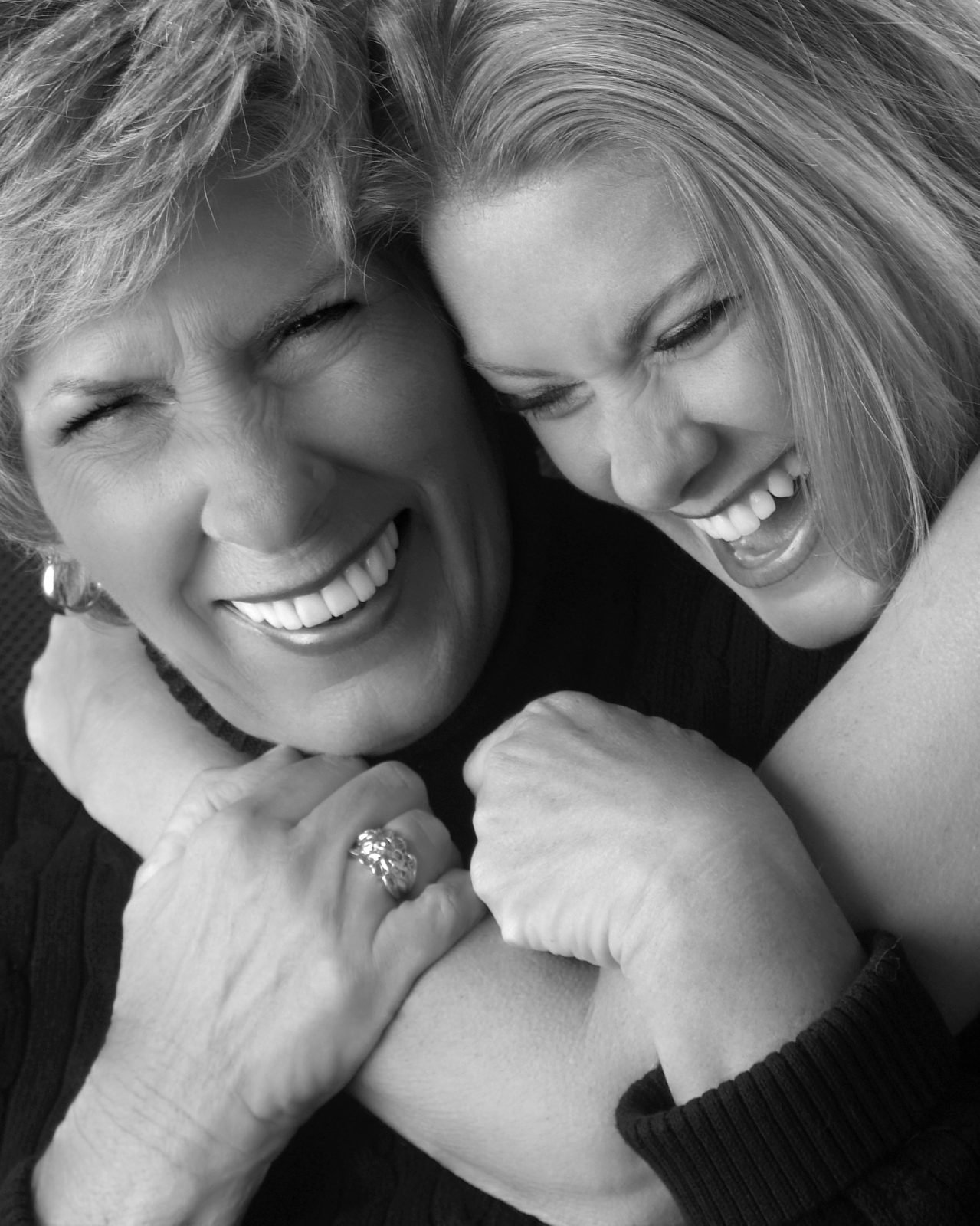 Two women hugging with wide smiles, close black and white portrait