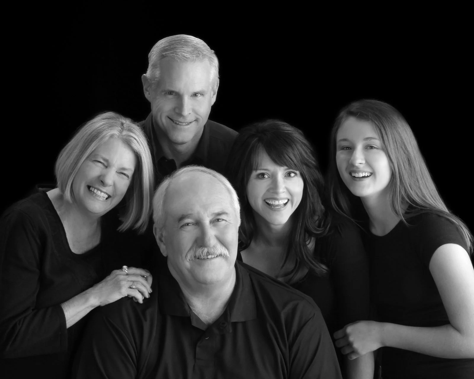Smiling multigenerational family of six posed together on a black backdrop, black and white portrait