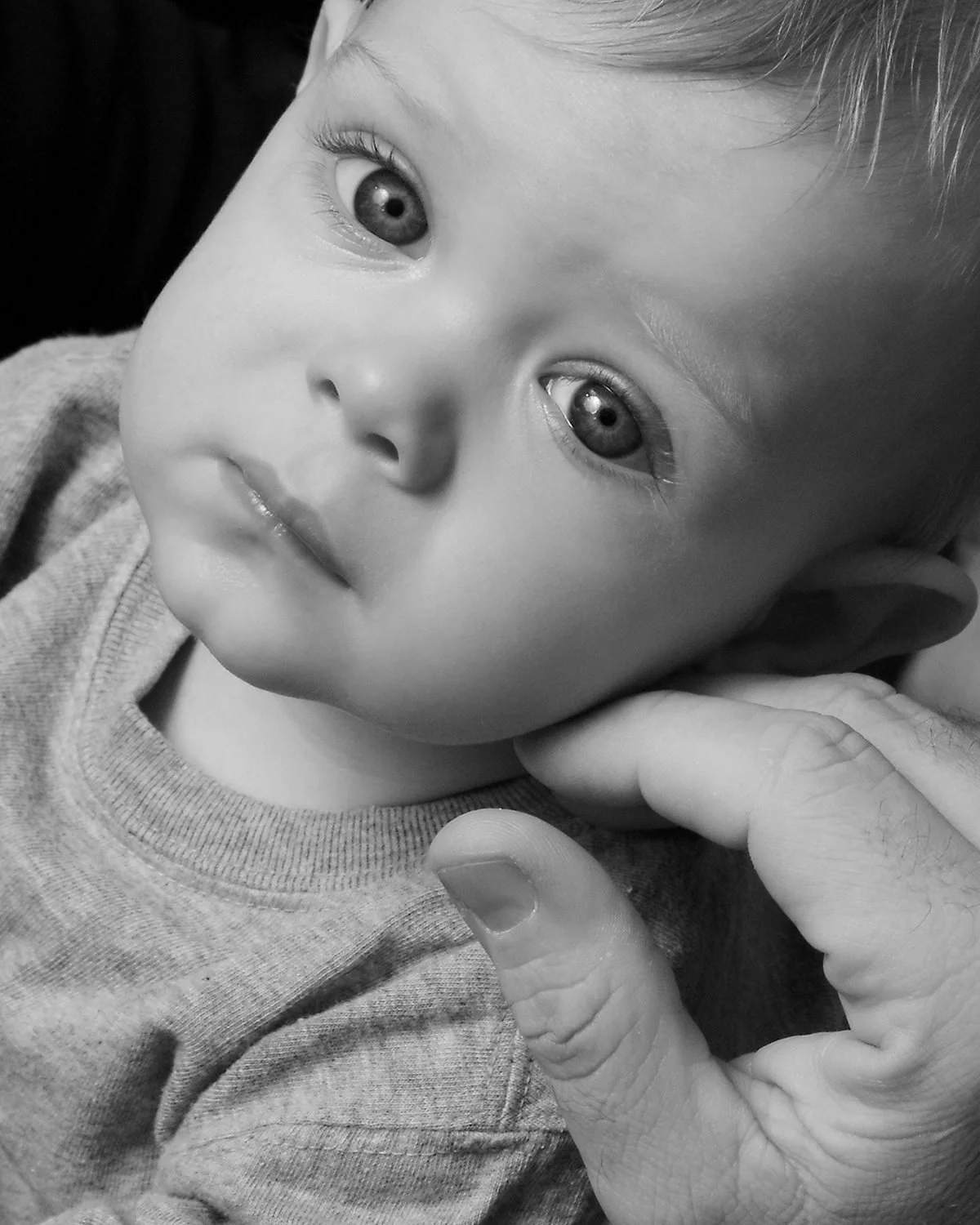 Close black and white portrait of a young child with wide eyes, held in a parent's hand, from the Soulmarks HEAL Project