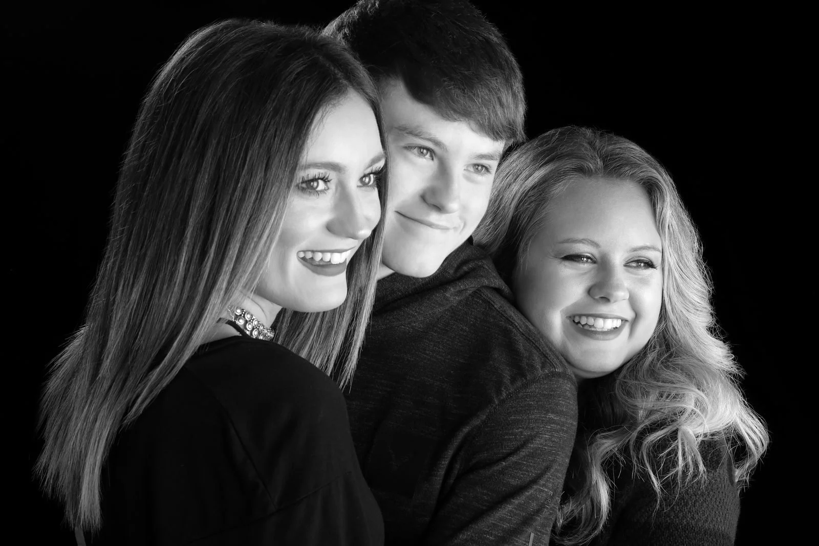 Three smiling young adults close together on a black backdrop, black and white portrait
