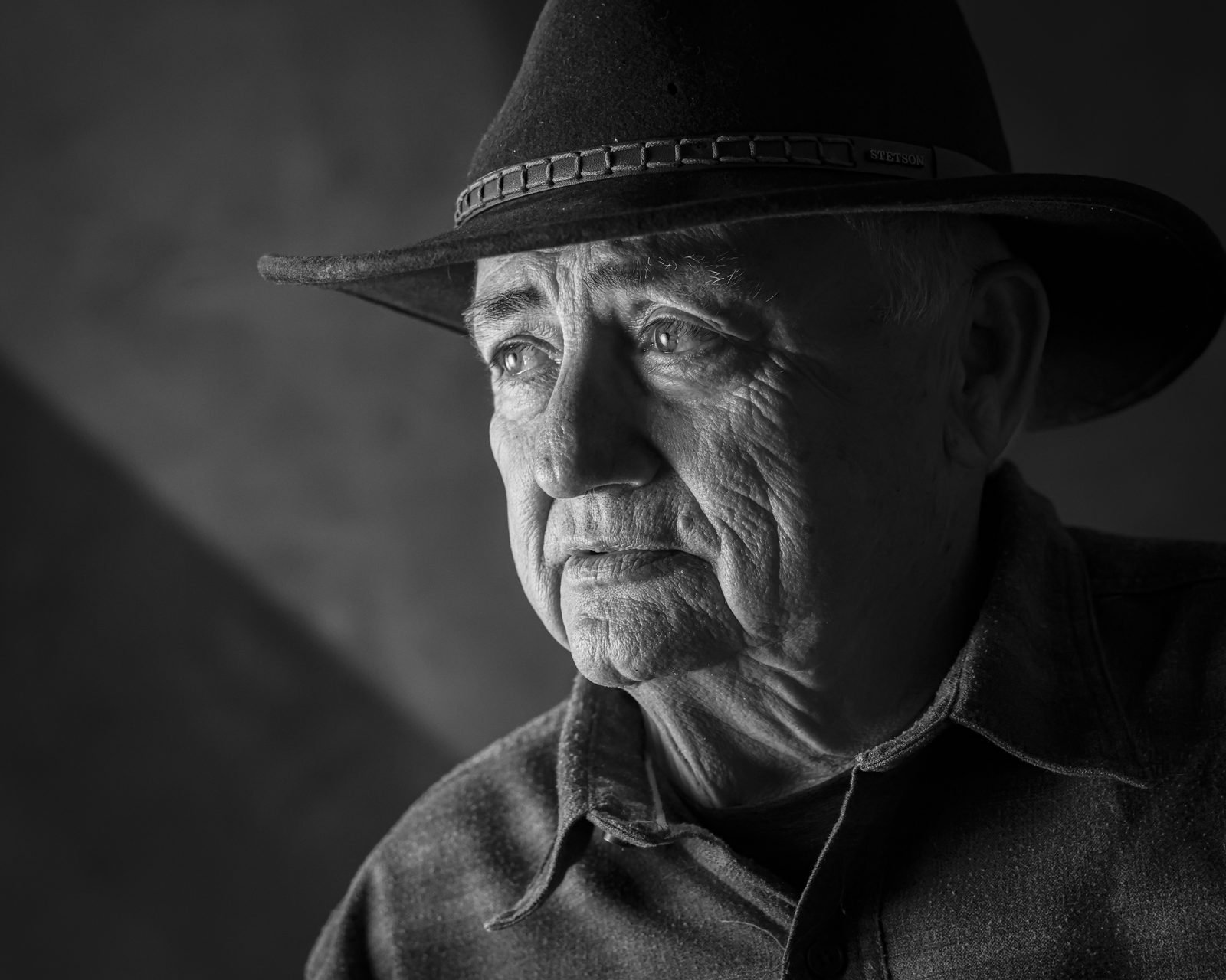 Black and white portrait of an older farmer in a wide-brimmed hat, looking thoughtfully to the side