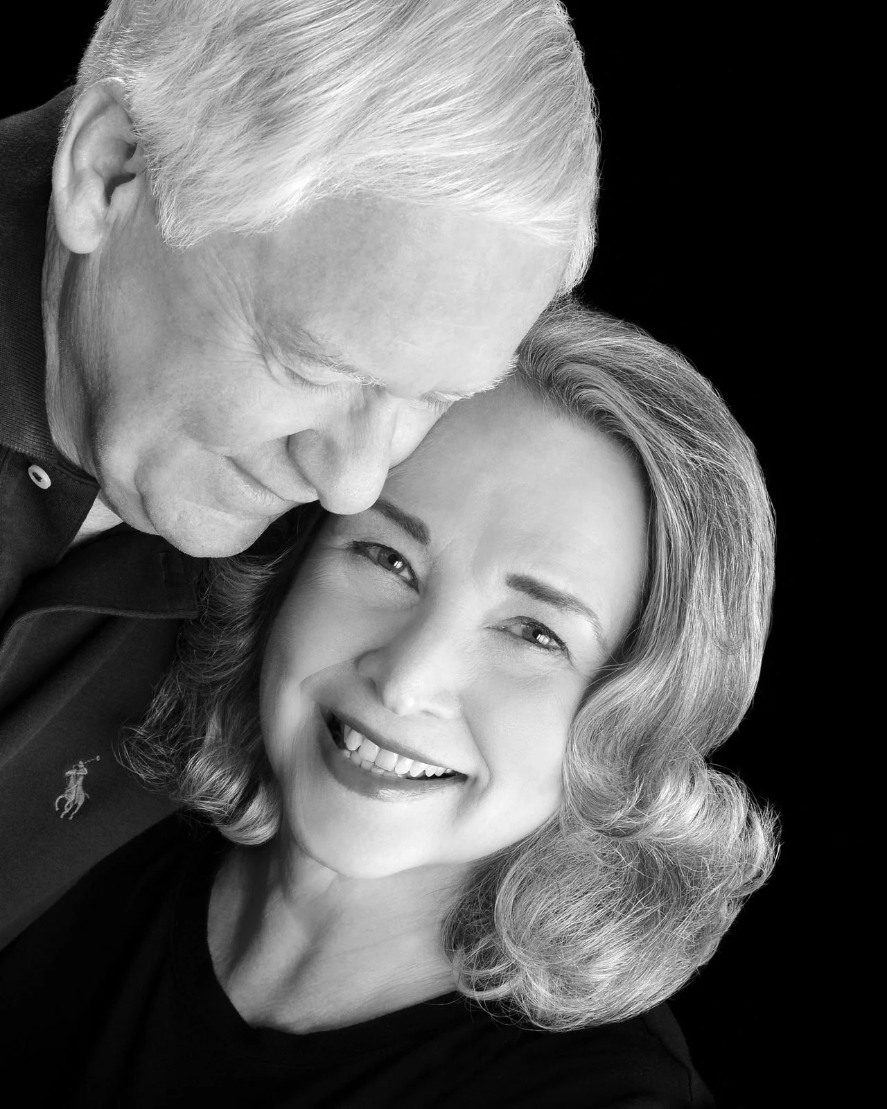 Older couple smiling close together, the husband resting his head against his wife, black and white portrait
