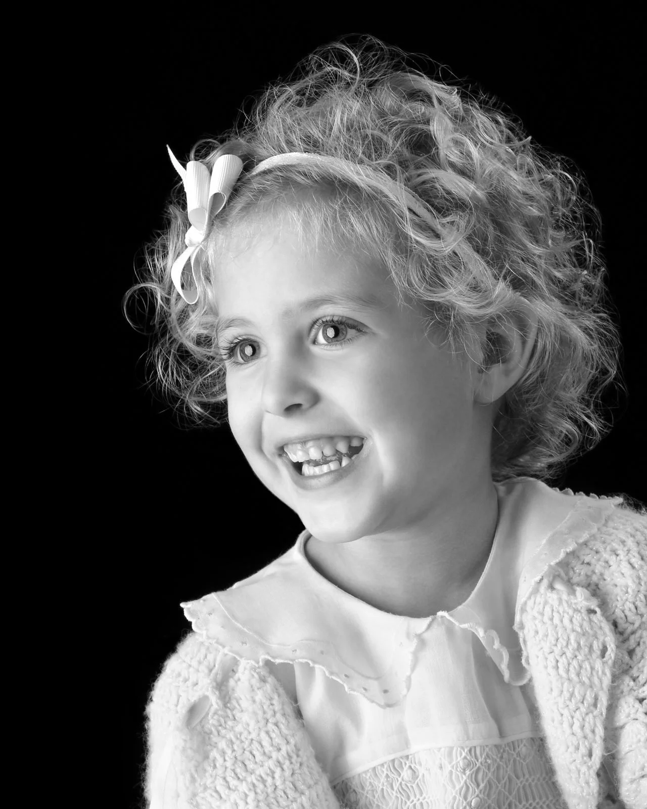 Smiling young girl with curly hair and a headband, black and white portrait