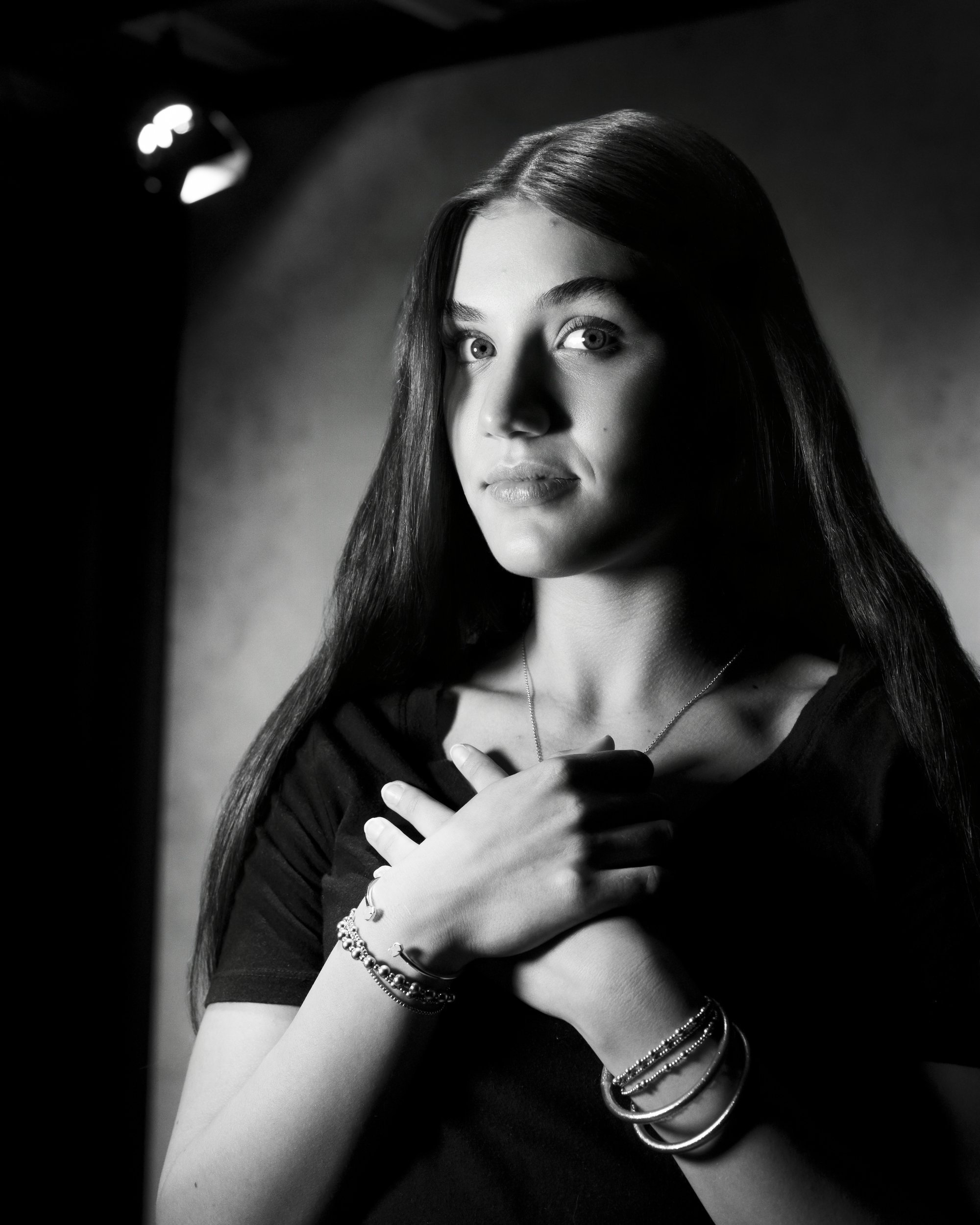 Black and white portrait of a teenage girl with her hands crossed over her chest, gazing into the camera