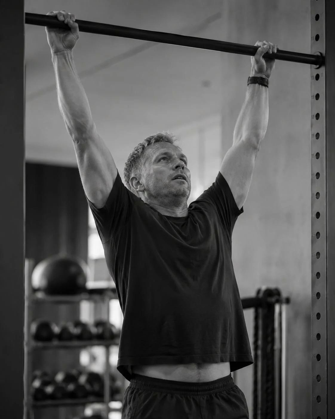 A man lifting a barbell overhead in a gym, black and white photo.