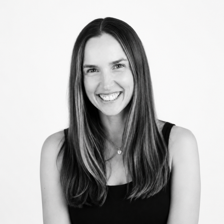A woman with long straight hair and a wide smile, wearing a black sleeveless top and a necklace, in front of a plain white background.