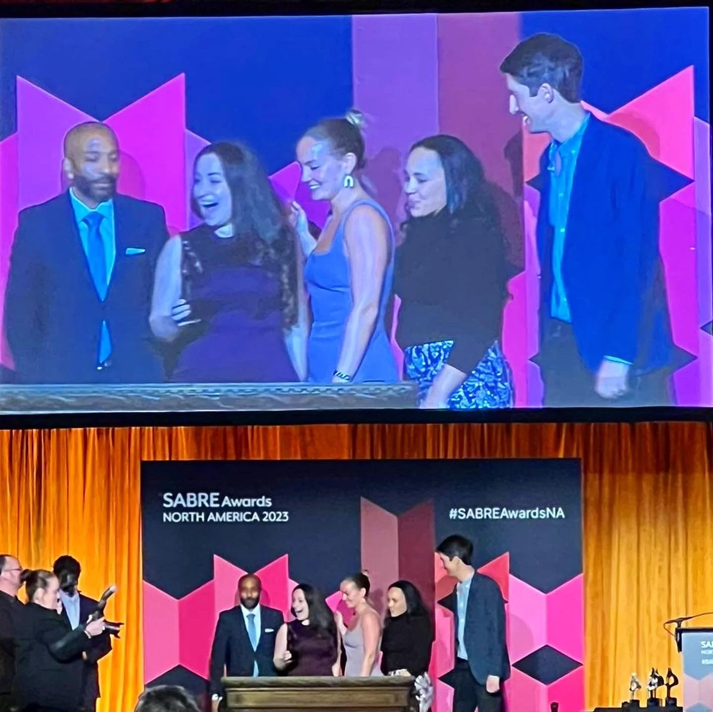 Group of people on stage at the SABRE Awards North America 2023, with a large screen displaying the event's name and hashtag. Some individuals are engaging in conversation and smiling.