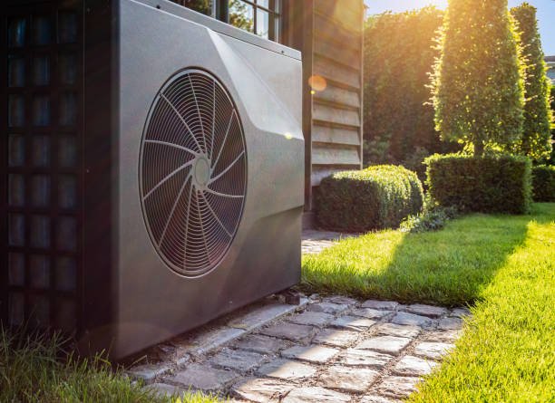Un'unità esterna di un sistema di riscaldamento o condizionamento vicino a una casa, con il sole che splende sul giardino ben curato.