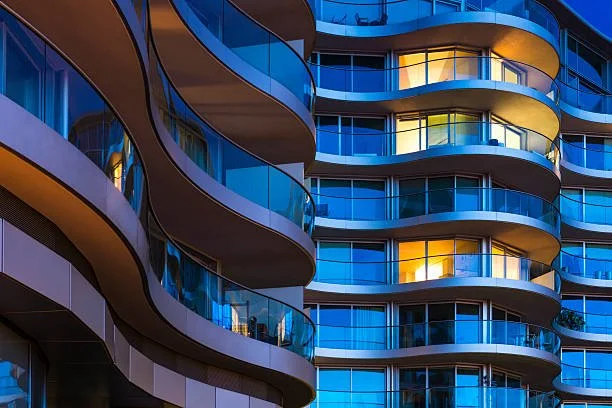 Edificio moderno con balconi ondulati e vetrate blu, illuminato dall'interno.
