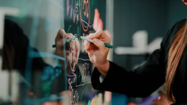 Una persona che scrive su una lavagna luminosa con un pennarello, con vari diagrammi e scritte colorate.