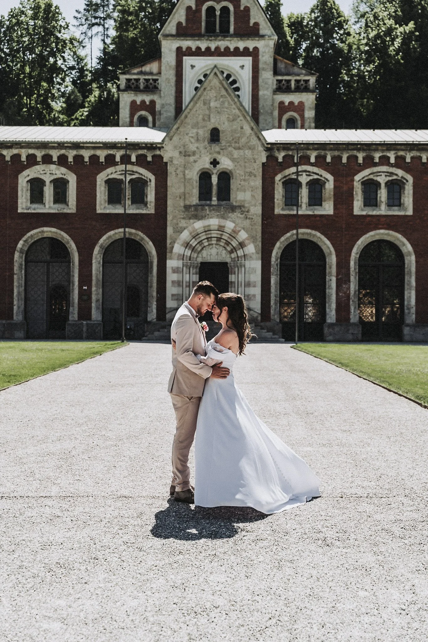 Ein Brautpaar, das sich vor einem historischen Gebäude aneinander lehnt, bei Sonnenlicht.