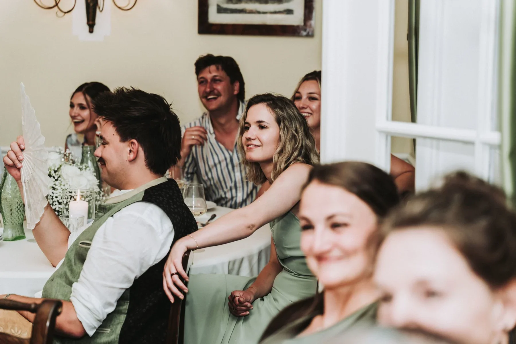 Freunde lachen gemeinsam am Hochzeitstisch.