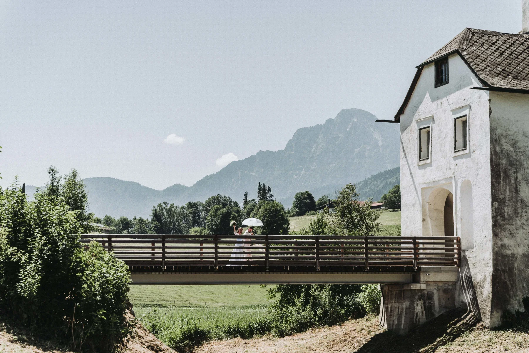 Brautpaar auf einer Brücke mit historischer Kirche im Hintergrund.