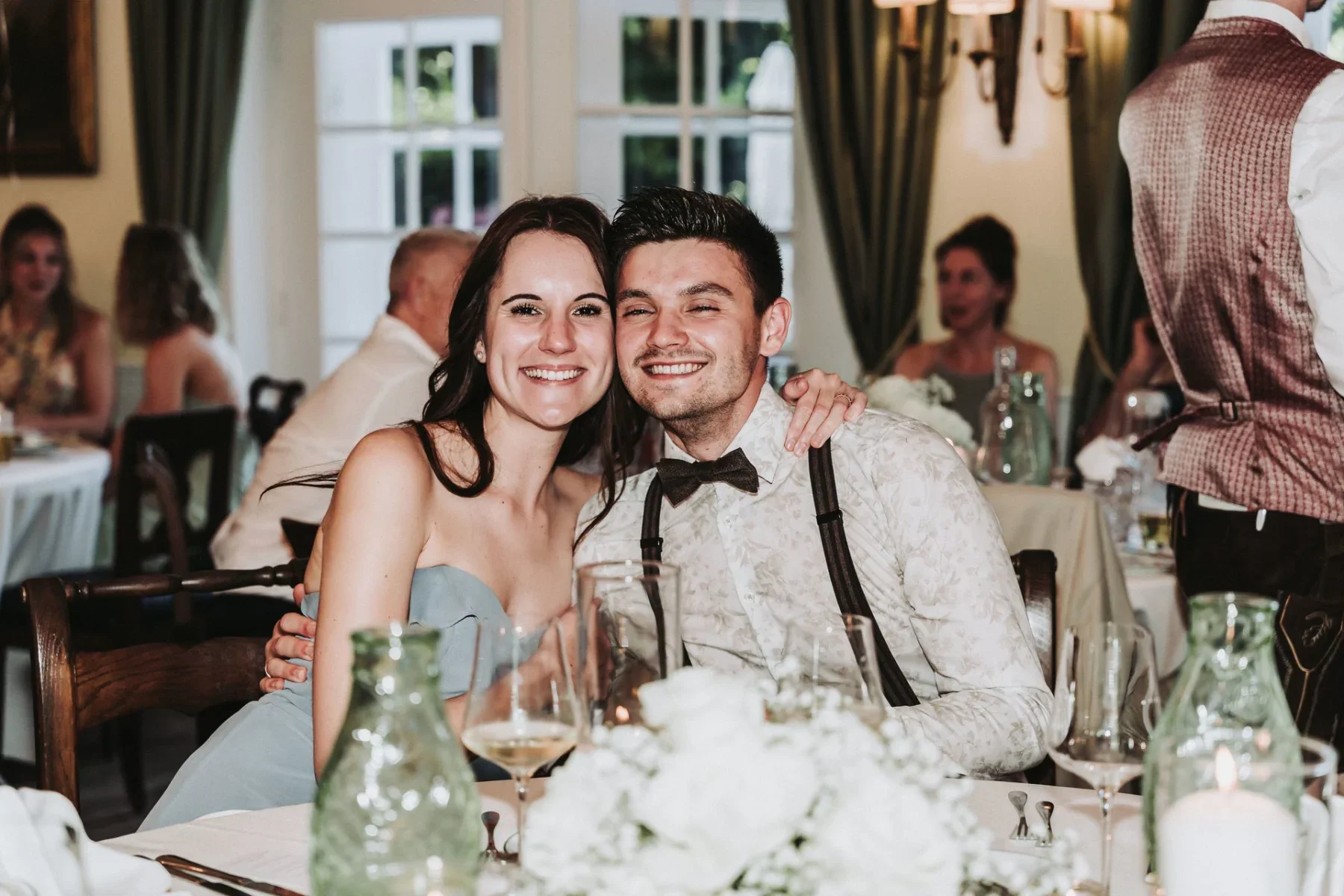 Das Brautpaar lächelt gemeinsam am Hochzeitstisch.