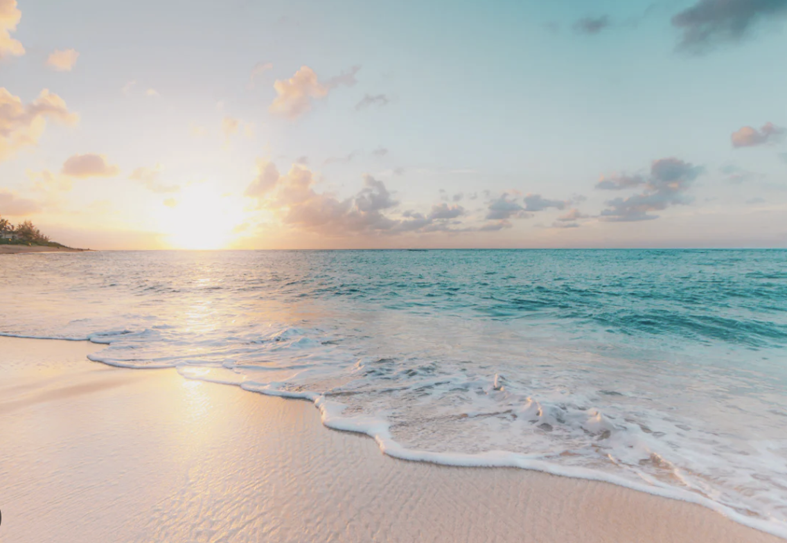 Sunset at the beach with calm waves, sandy shore, and a partly cloudy sky.