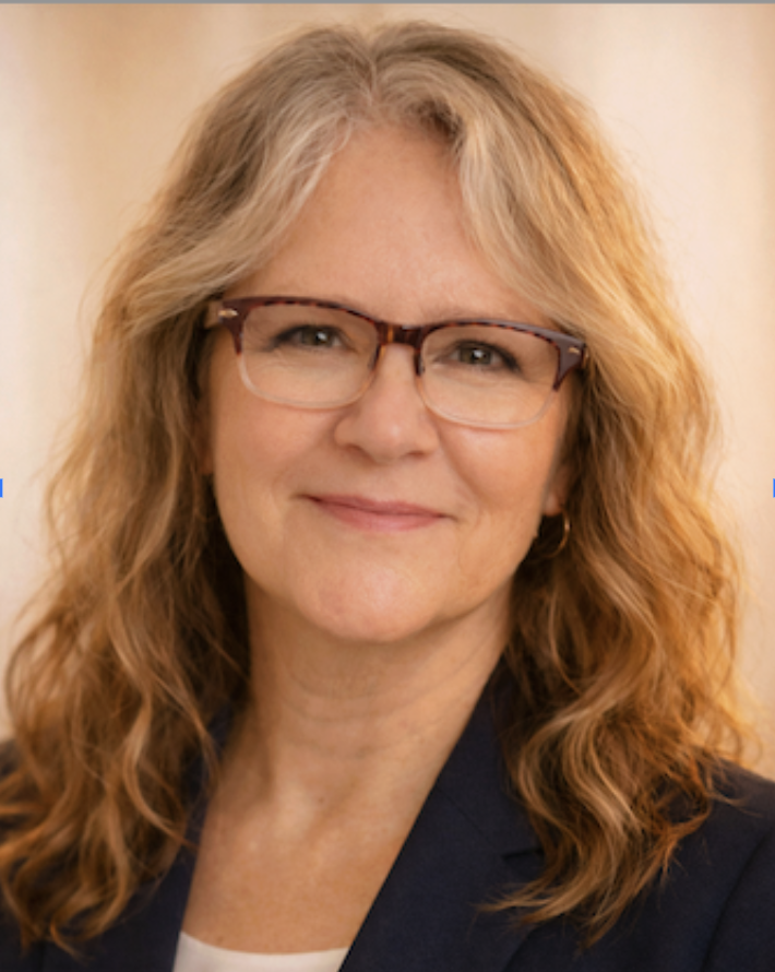 A woman with wavy blonde hair and glasses smiling at the camera.