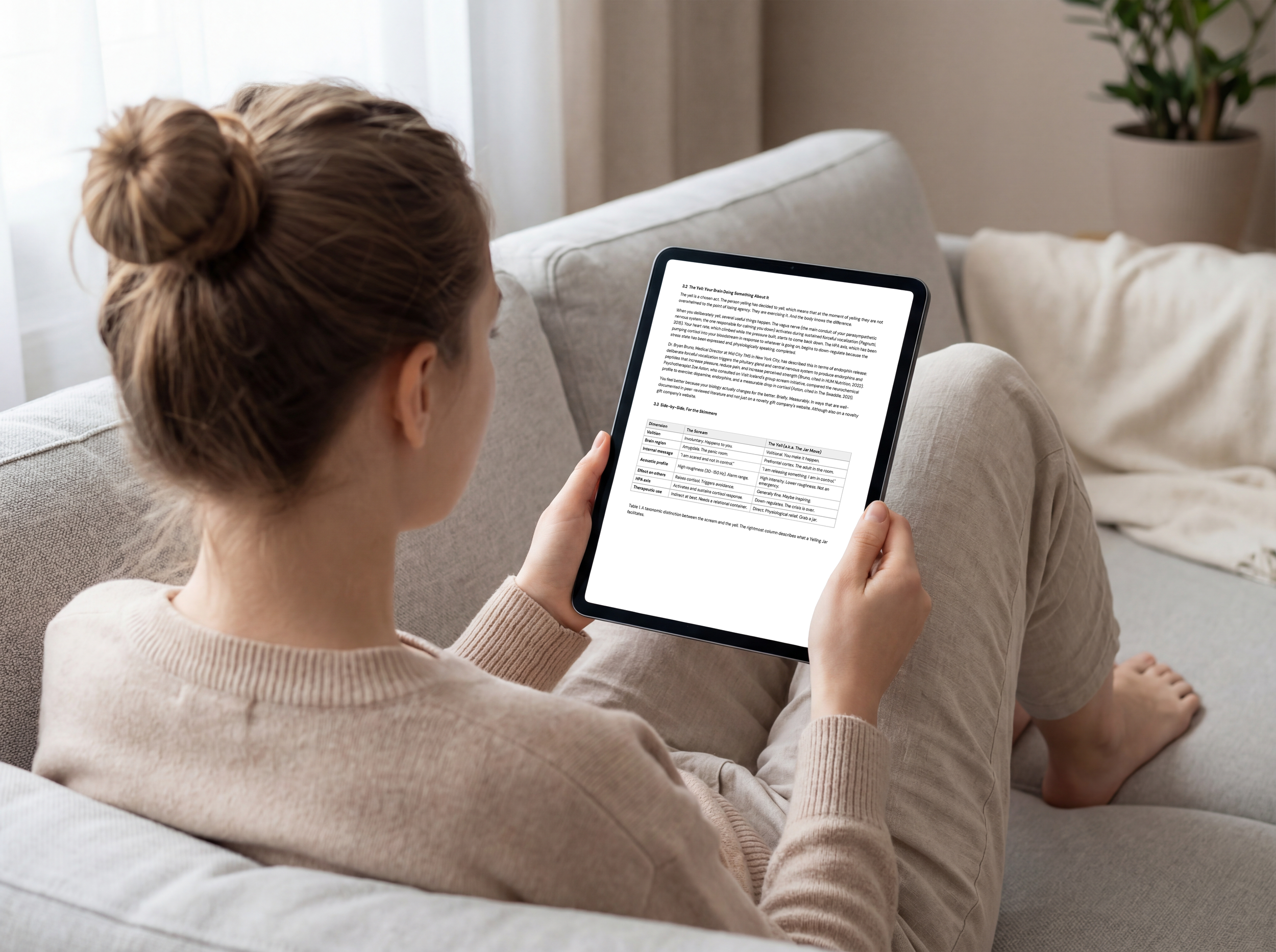 woman sitting on plush couch with large tablet reading page three of the yelling jars whitepaper.