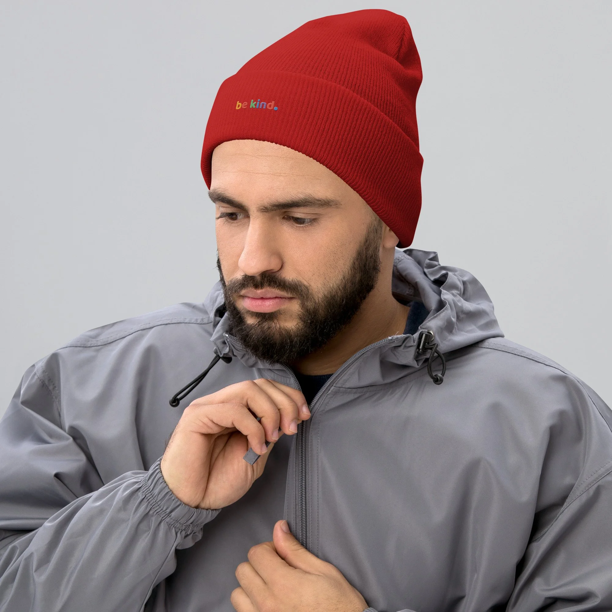Man in a grey jacket looking down, wearing a red be kind cuffed beanie