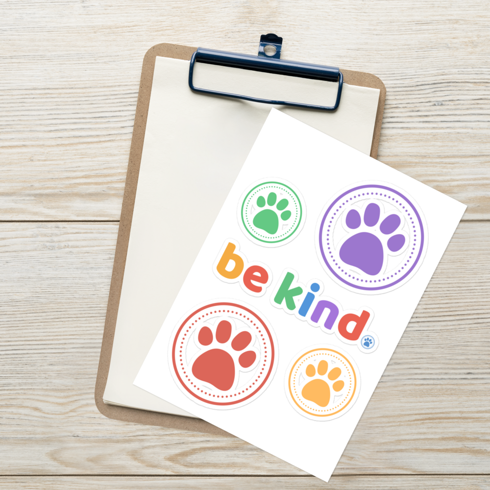 The be kind sticker sheet resting on a clipboard on a white wood surface