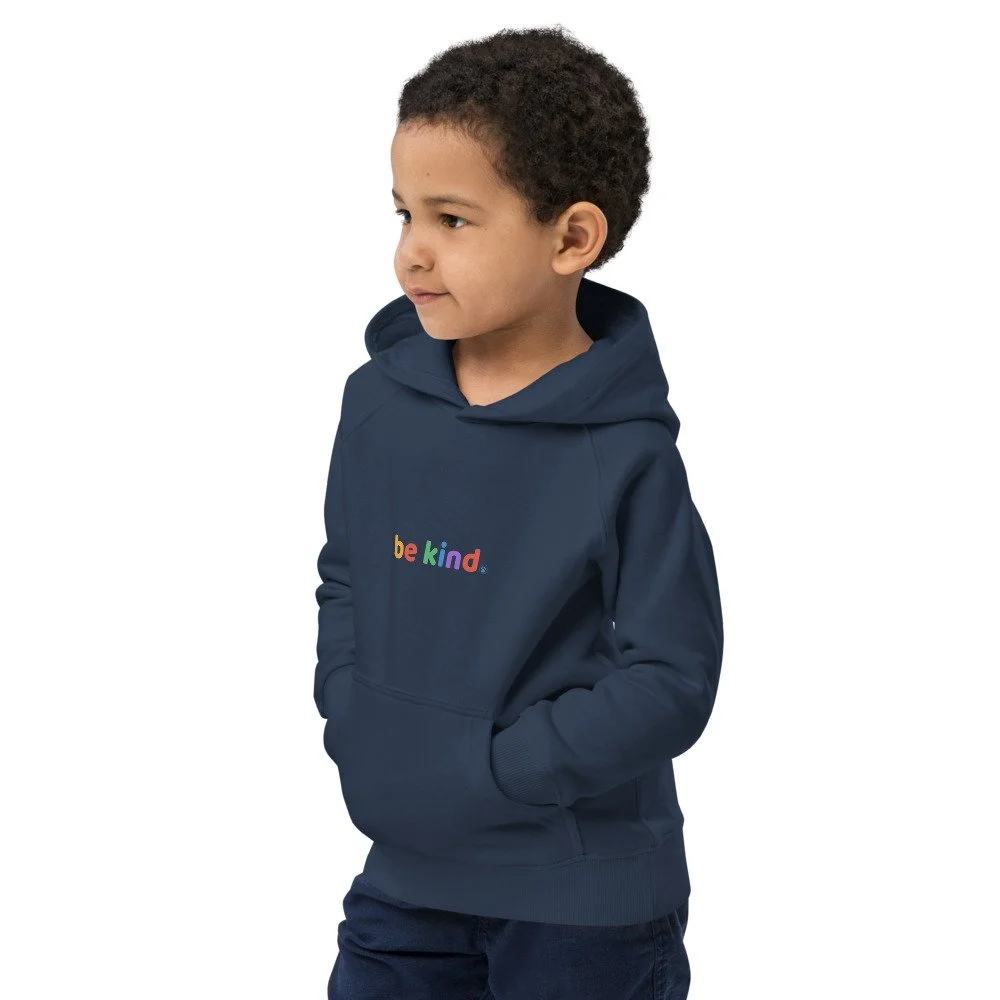 Boy in a navy be kind hoodie turned to the side with his hands in the front pouch