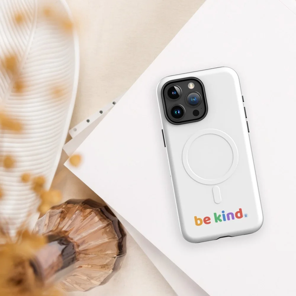 Be Kind MagSafe iPhone 15 Pro Max case angled on white paper beside dried flowers