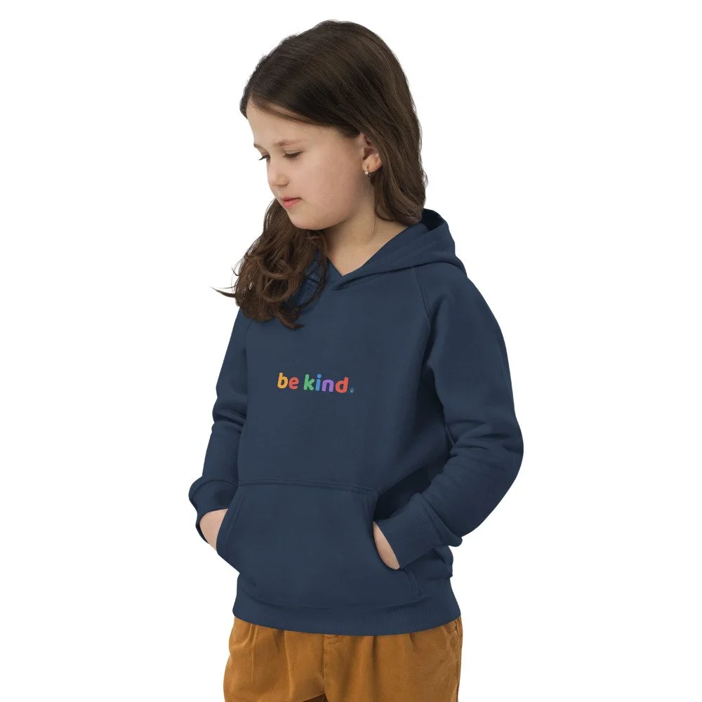 Girl in a navy be kind hoodie looking down with her hands in the front pouch