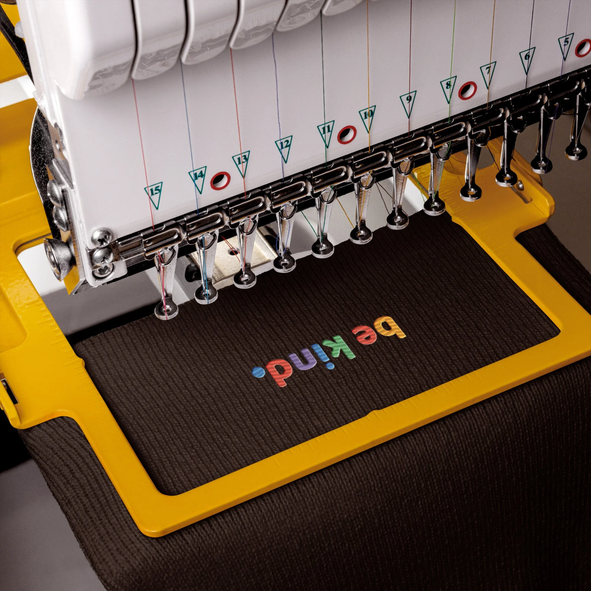 Brown cuffed beanie in an embroidery machine as the rainbow be kind mark is stitched onto the cuff