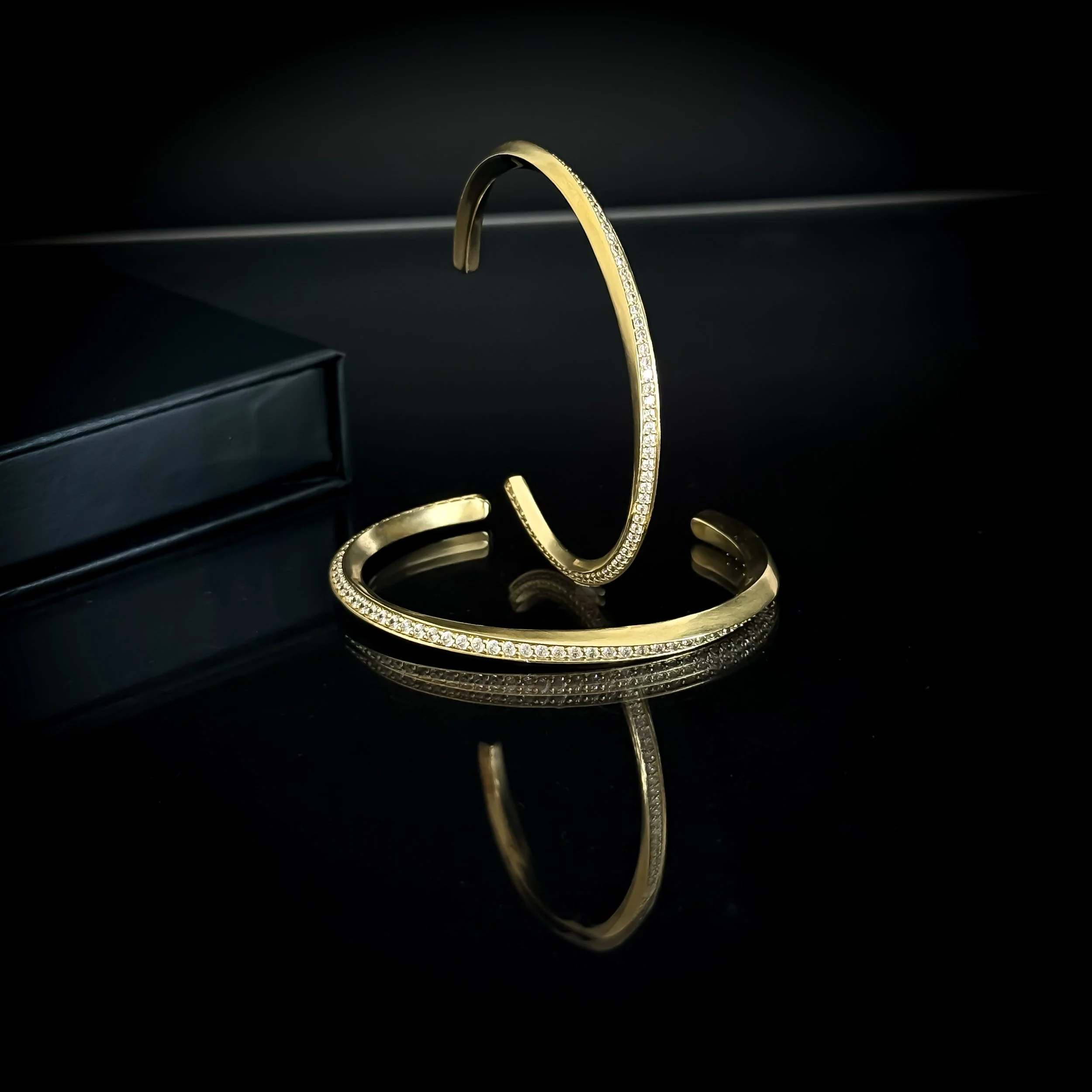 A gold jewelry bracelet and a gold necklace with diamonds, reflecting on a black surface.