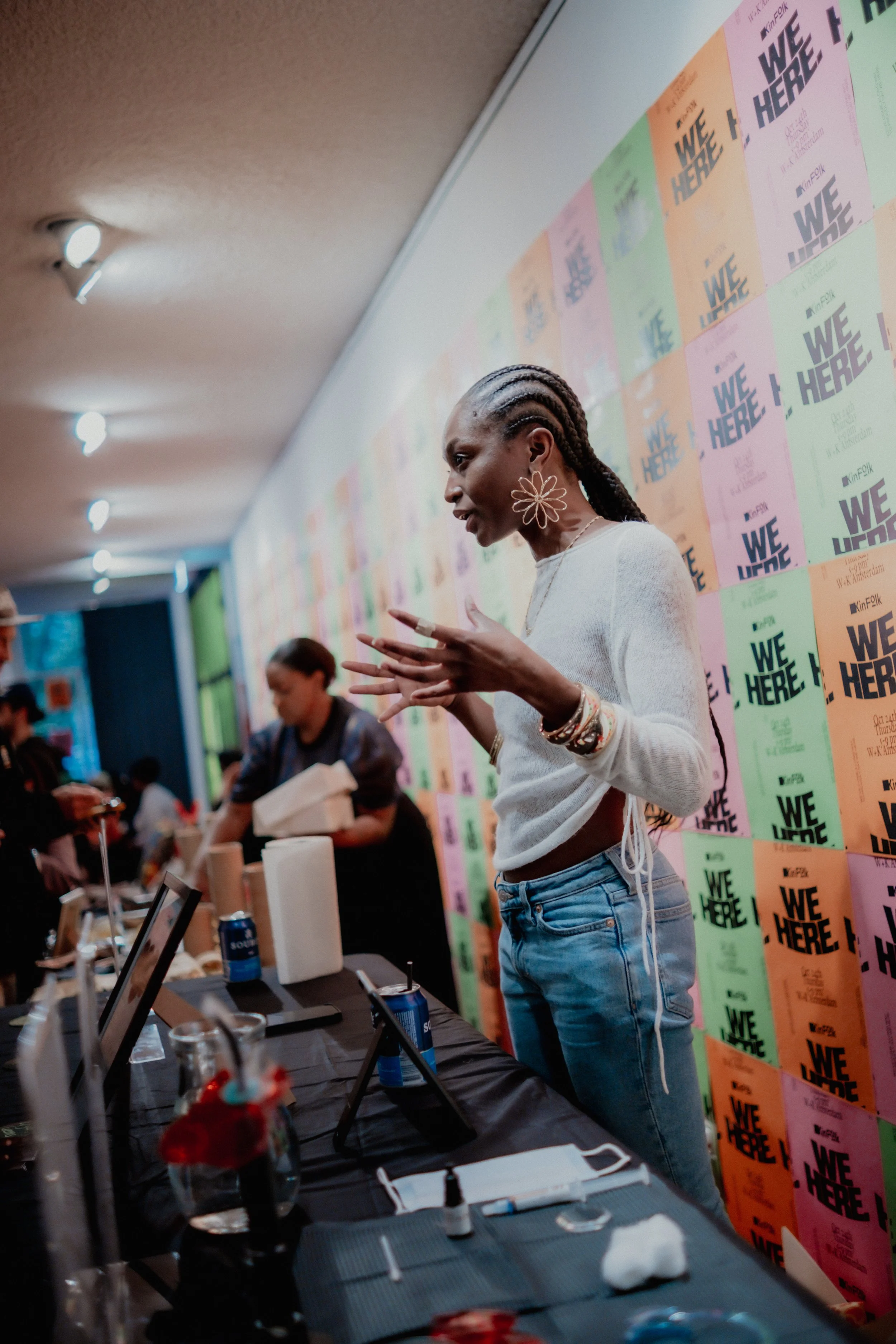 A woman with braided hair and large flower-shaped earrings speaking at an event with a colorful 