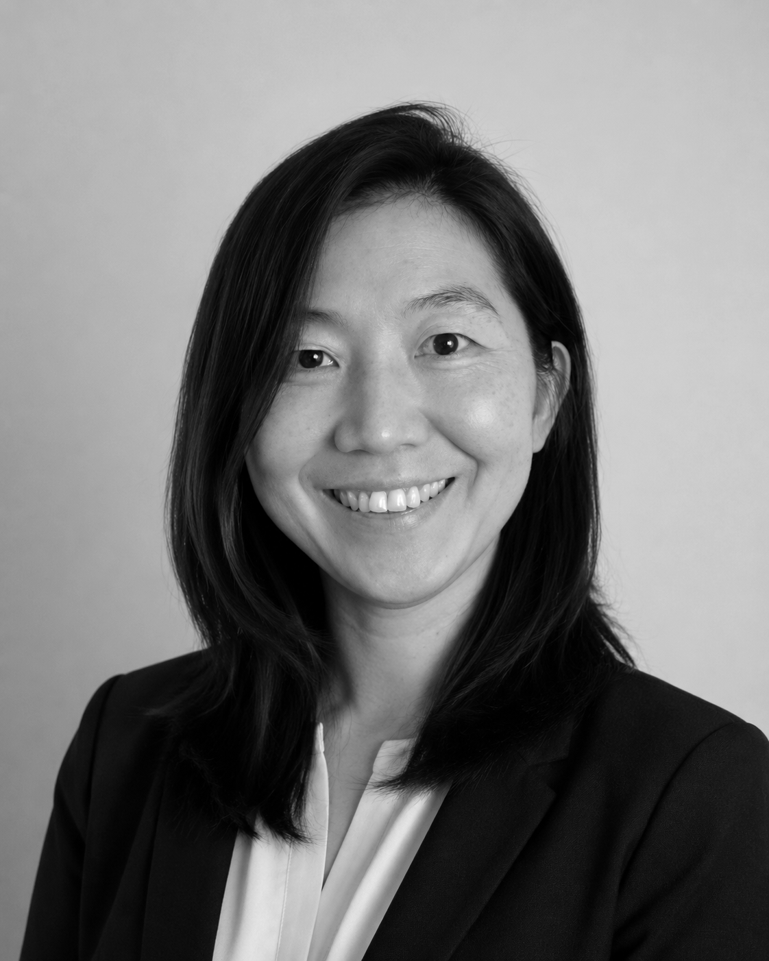 Black and white portrait of a smiling woman with shoulder-length dark hair wearing a dark blazer and white blouse.