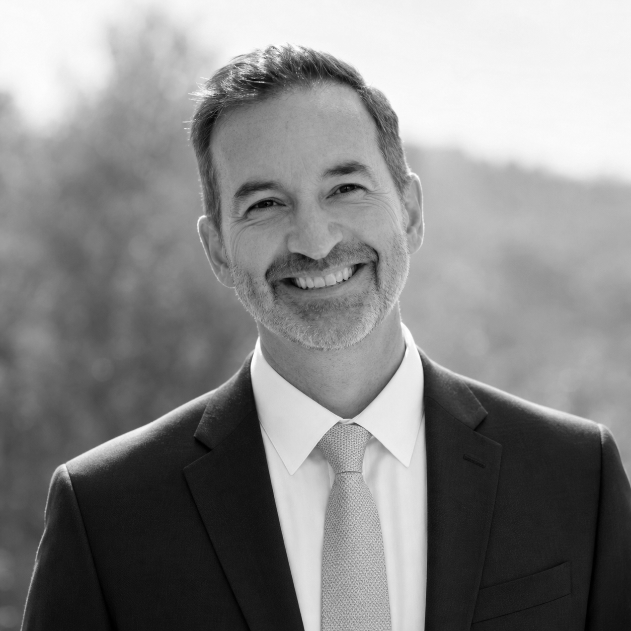 Black and white portrait of a smiling man wearing a suit and tie outdoors.