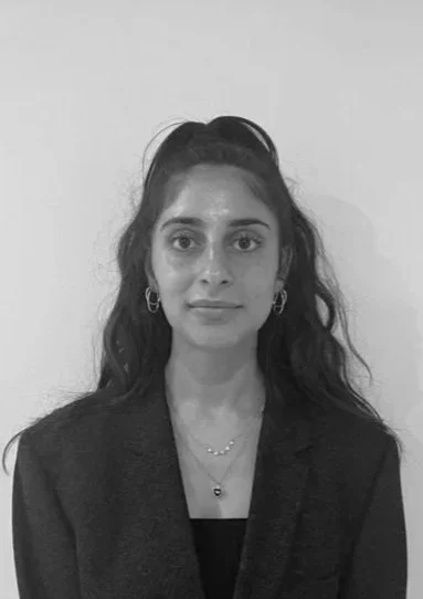 Black and white portrait of a woman with long wavy hair, wearing a blazer and jewelry, facing the camera with a neutral expression.