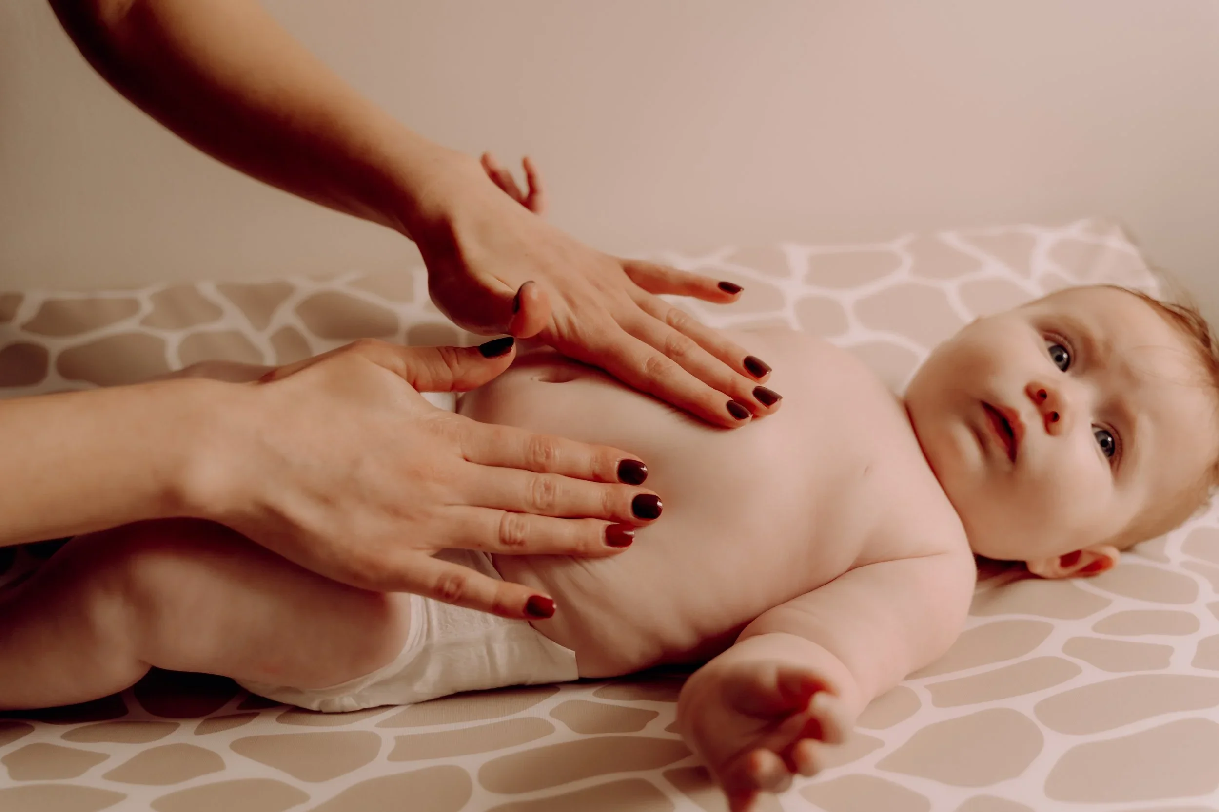 A child lying on a bed with hands of two adults pressing on their back, appearing to receive a massage or therapy.