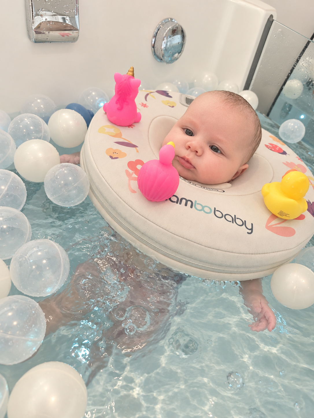 Baby floating in a baby spa with a neck float and sensory toys