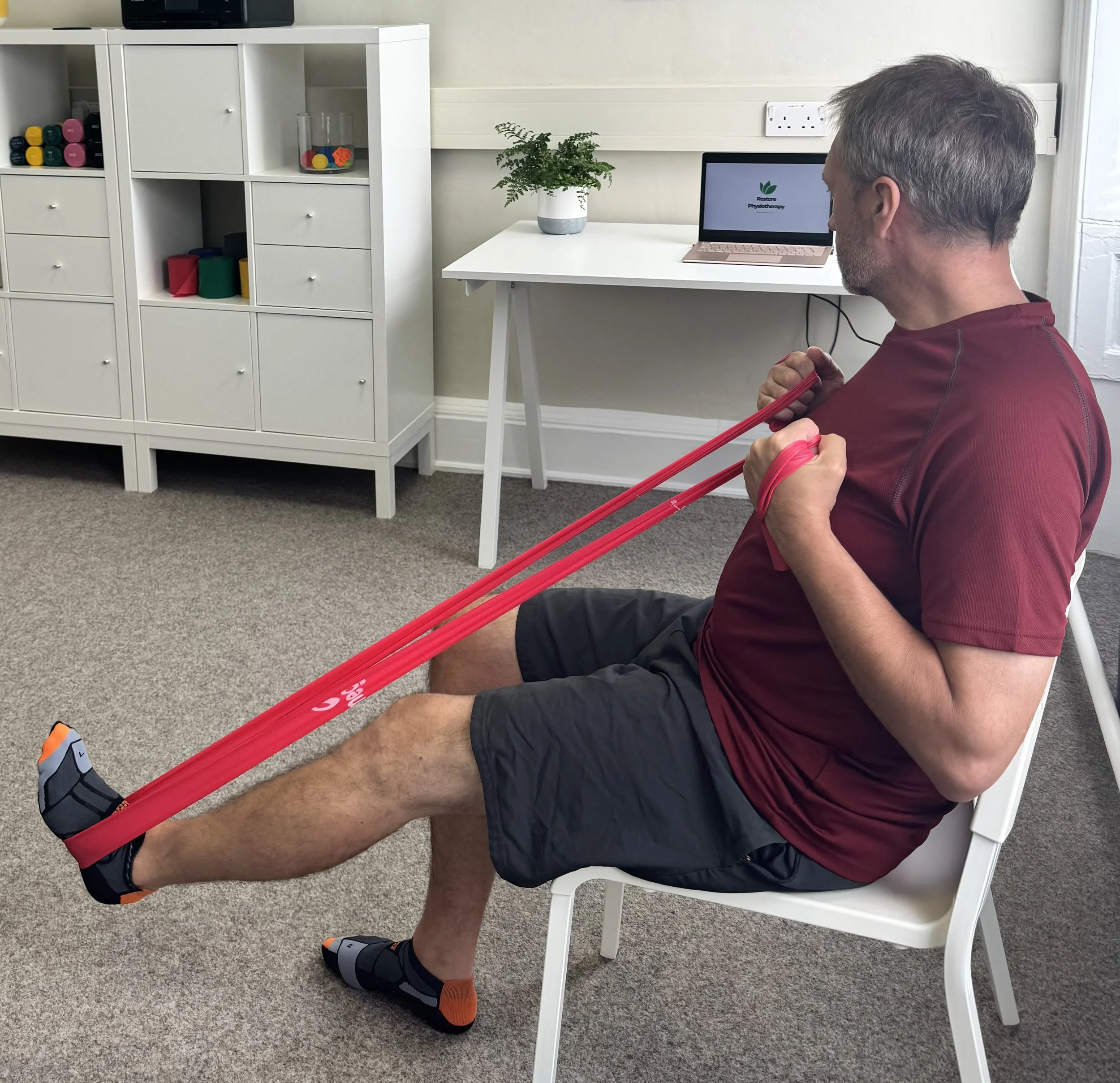 Person performing a seated leg press with a resistance band under physiotherapy supervision